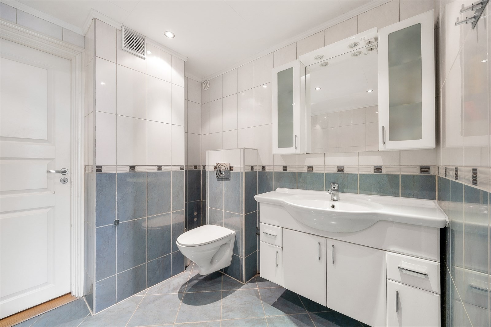 Den første badet er utstyrt med badekar med dusj og glassvegg, vegghengt wc og servantinnredning med skuffer, under- og overskap Galleribilde