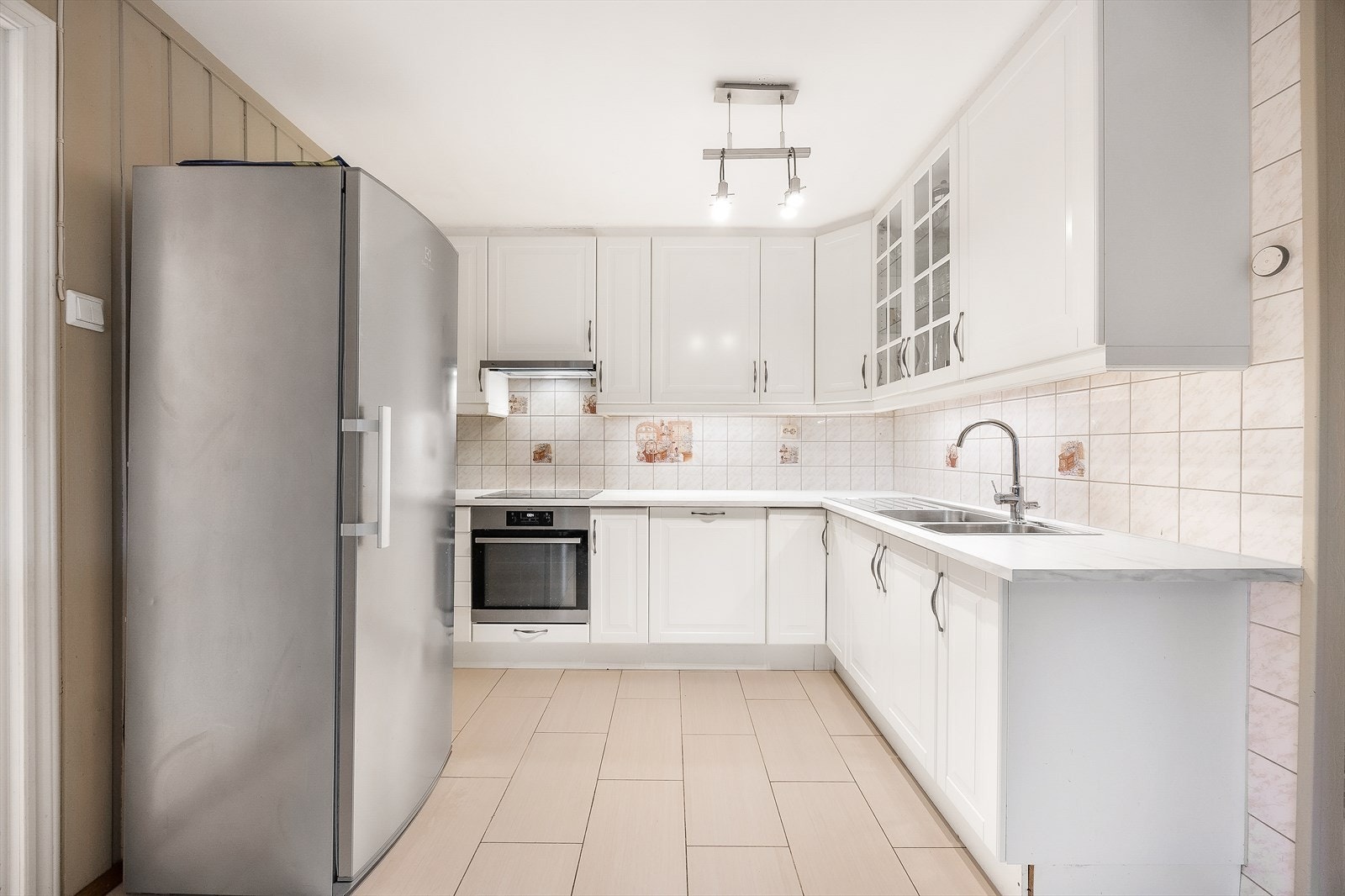 Innredningen har hvite profilerte fronter, vitrineskap og laminerte benkeplater. Nyere kjøkkenfronter, vask, kran og kjøkkenvifte Galleribilde