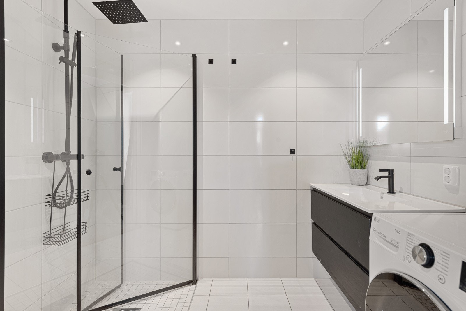 Badet har dusjhjørne med glassdører, toalett, servantskap og opplegg for vaskemaskin Galleribilde