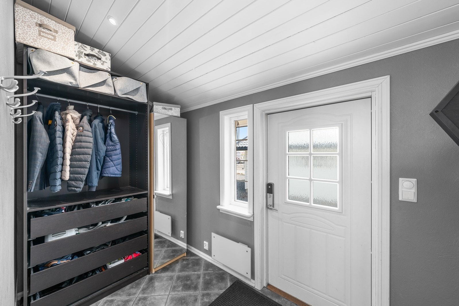 På innsiden har entreen grå fliser med vannbåren gulvvarme, gråmalte vegger og skråhimling med hvitmalt panel og downlights. Galleribilde