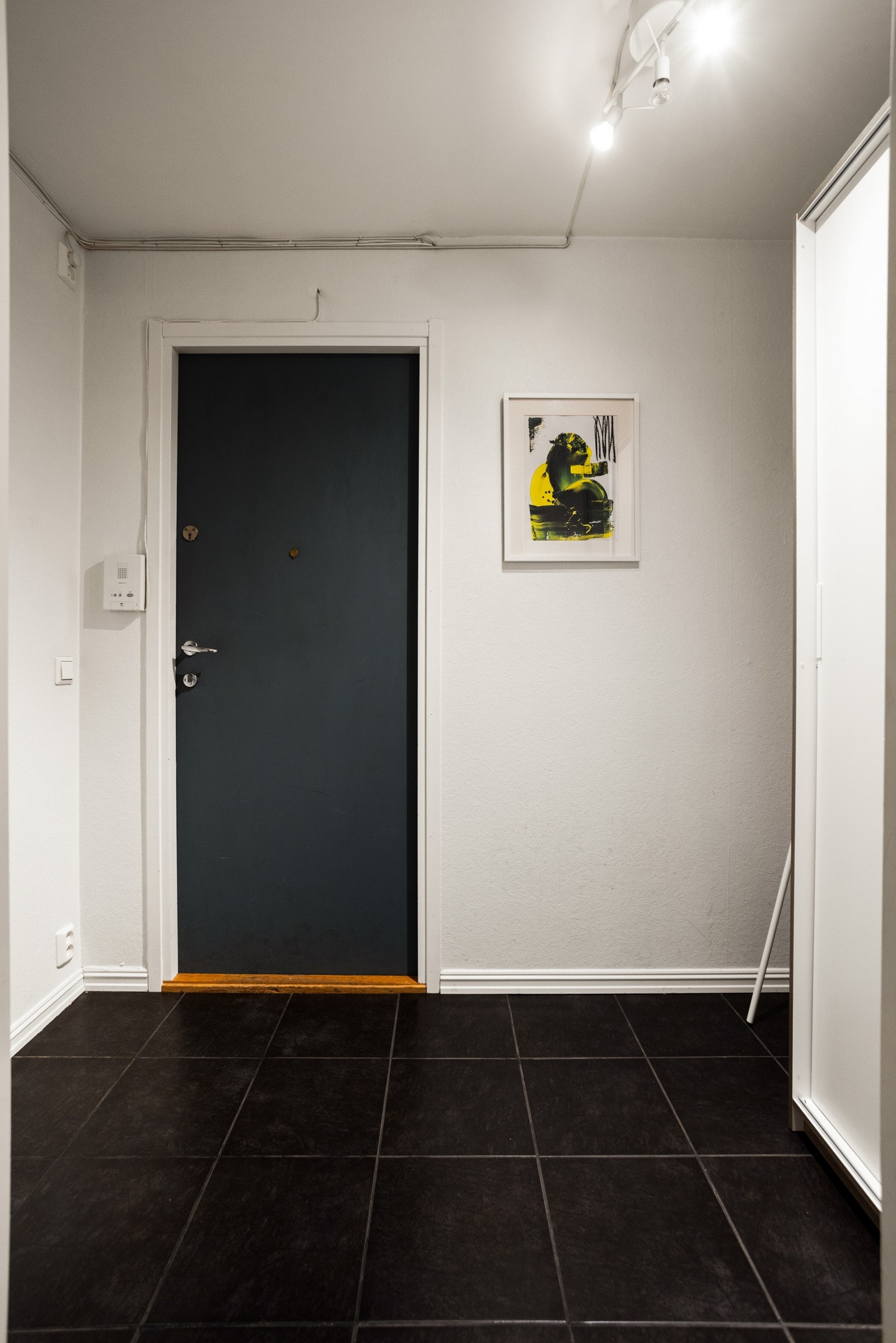 Entreen er innredet med hvitmalte vegger og store, sorte fliser på gulvet Galleribilde