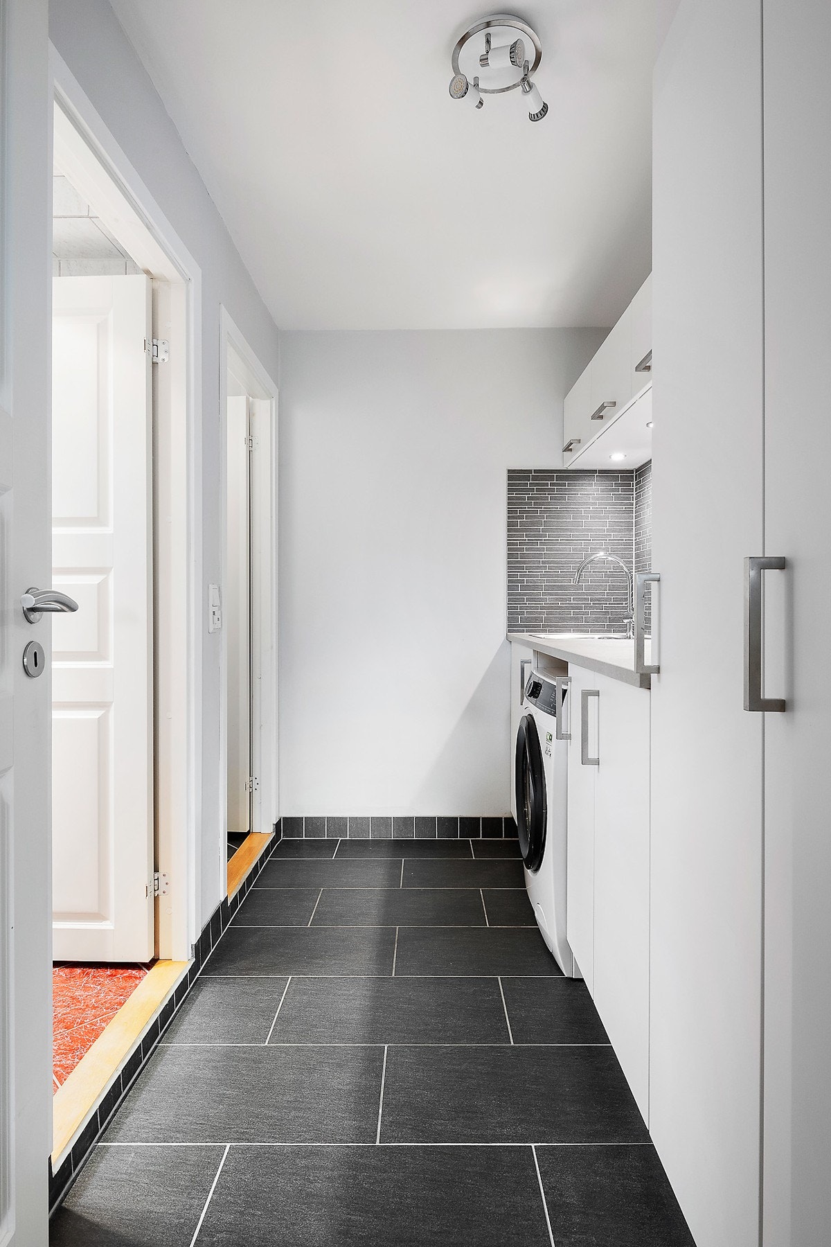 Rom innredet som vaskerom fra 2015. Gulvflate er belagt med fliser. Innredning med slette fronter, benkeplate av laminat, vedfelt utslagsvask med ett-greps armatur. Fliser på vegg over benkeplate. Opplegg for vaskemaskin. Galleribilde