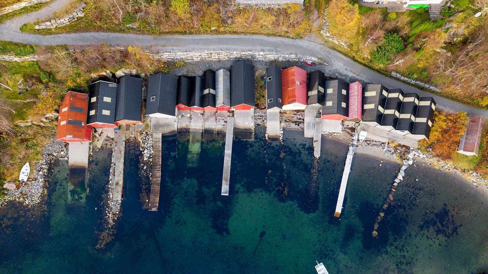 Dronebilde av naustrekka sett fra fugleperspektiv. Det er ei ubebygd nausttomt øst for naustet Galleribilde