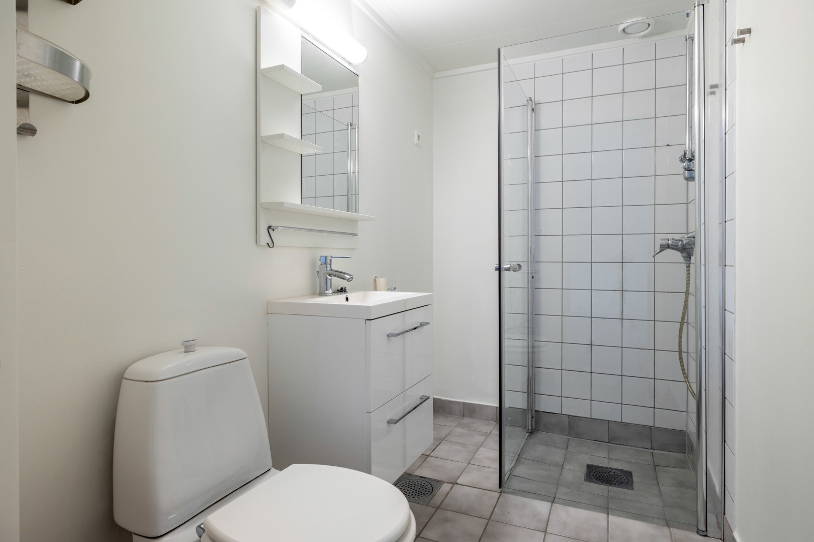 Leiligheten har et flislagt bad med moderniseringsbehov. Badet har dusjhjørne, gulvmontert toalett, servantinnredning med to skuffefronter og opplegg for vaskemaskin Galleribilde