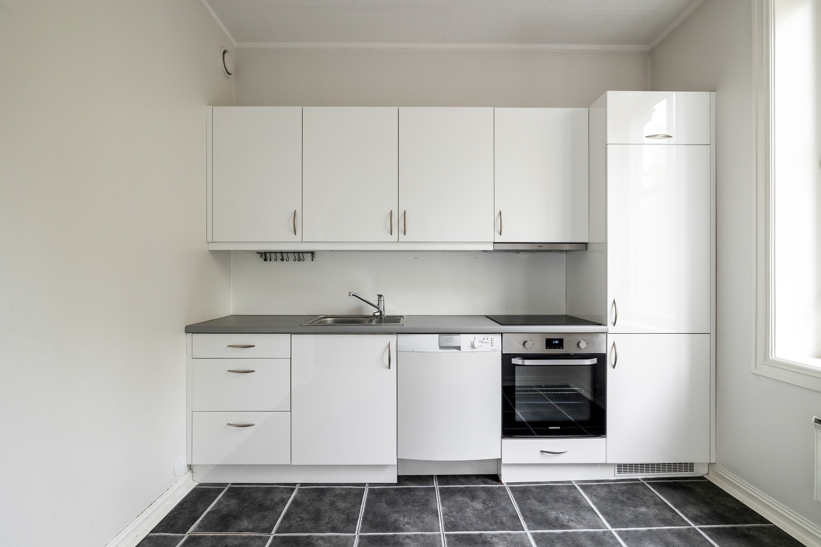 Kjøkkeninnredningen har glatte hvite fronter og laminat benkeplate med nedfelt kum i rustfritt stål Galleribilde