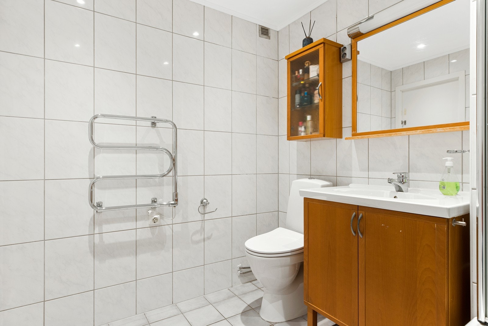 Baderom med fliser på vegg og gulv. Det er skap under servant og veggskap med plass til baderomsartikler. Baderommet har ukjent alder Galleribilde