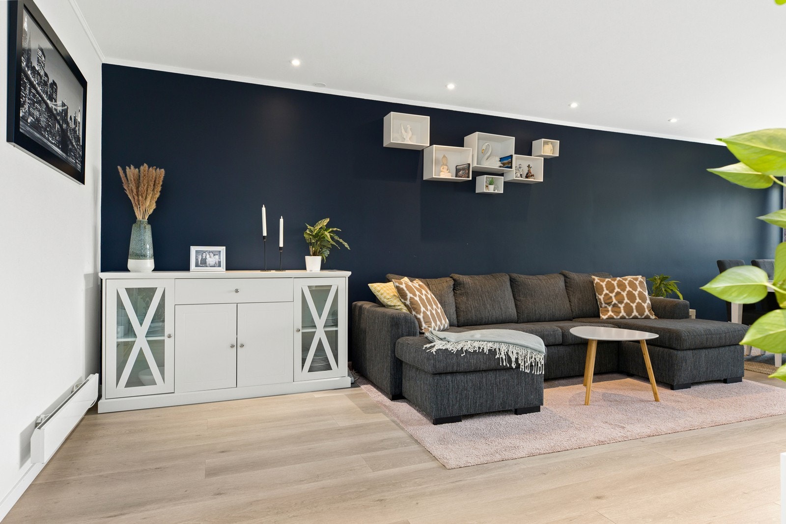 Det er en luftig stue med plass til både sofagruppe og spisestue. Langveggen er malt i en dyp blå farge som setter karakter på rommet Galleribilde