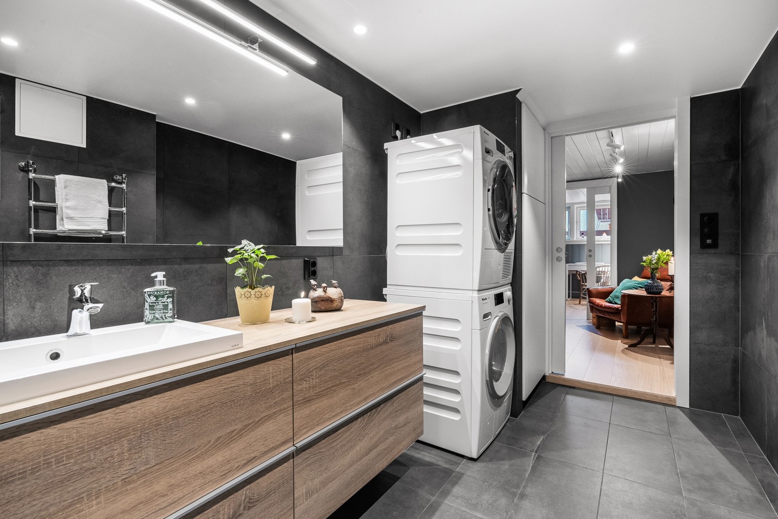 Badet har veggmontert servantskap med nedfelt keramisk vask og ett-greps armatur i krom. Det er tilrettelagt for både vaskemaskin og tørketrommel, noe som gjør rommet funksjonelt i hverdagen Galleribilde