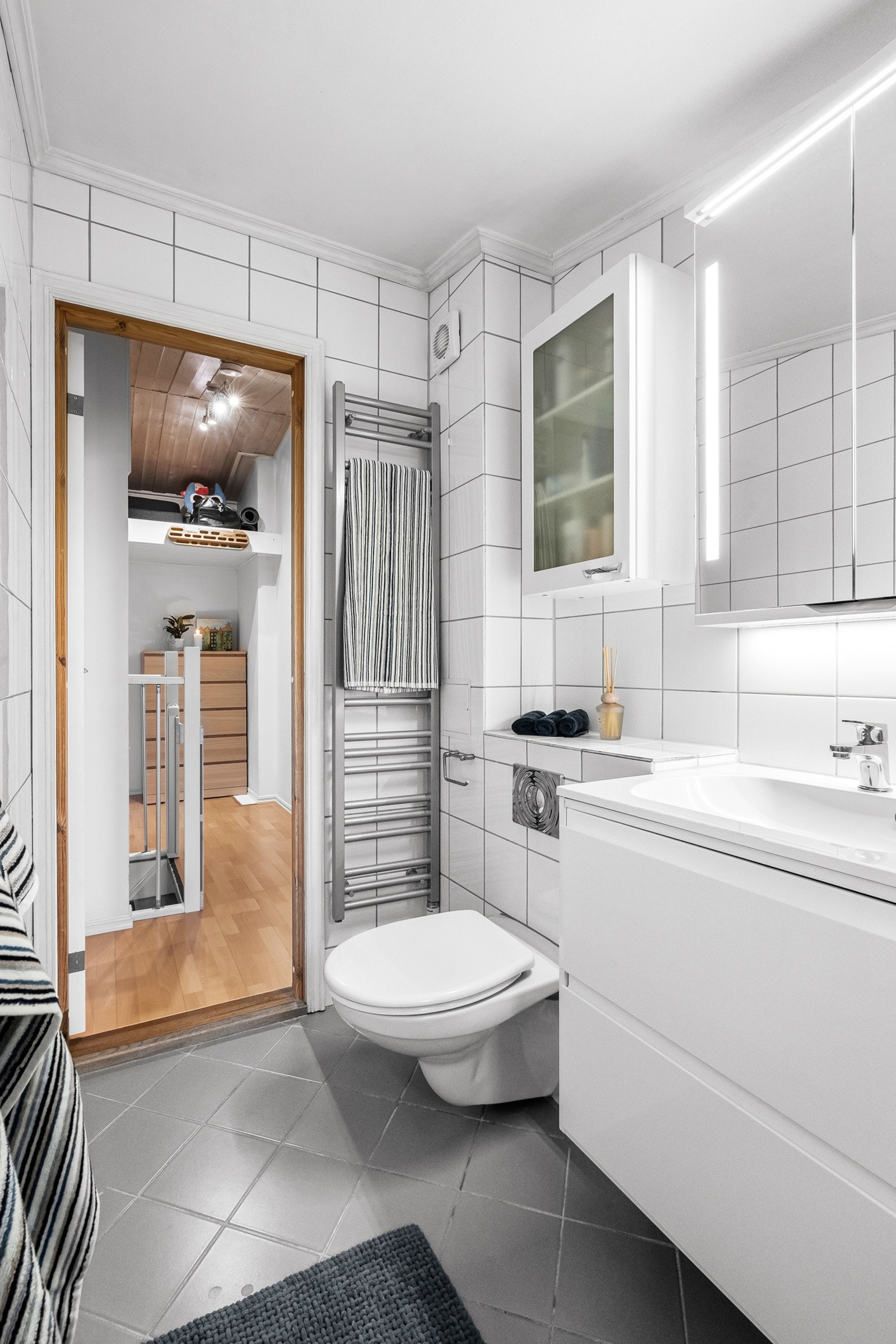 Romslig servantskap med veggmontert design og heldekkende vask, komplett med ett-greps armatur i krom. Over vasken finner du et praktisk speilskap med integrert belysning Galleribilde