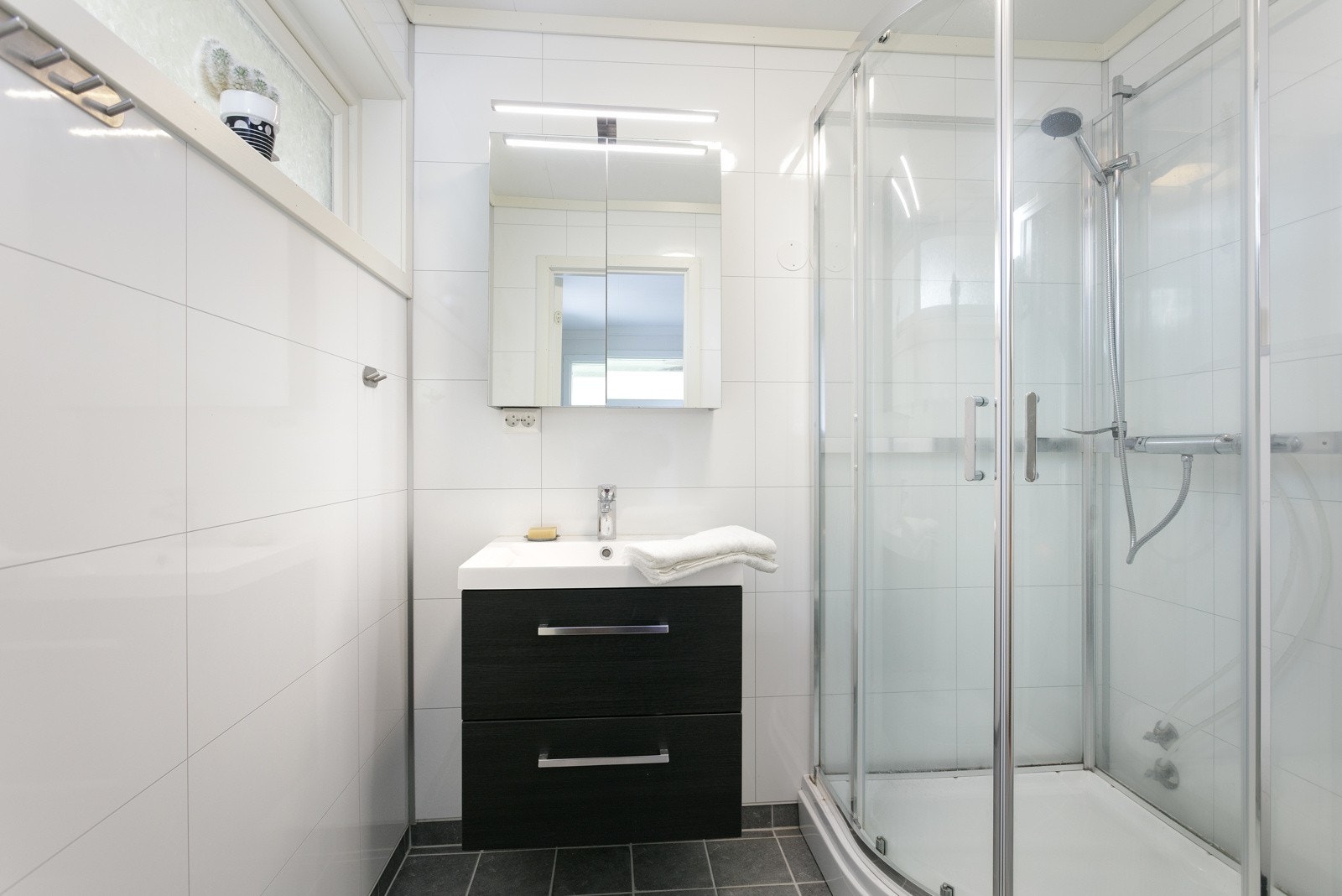 Boligen har to bad og her er badet i hovedetasjen som har dusjkabinett og servantinnredning Galleribilde