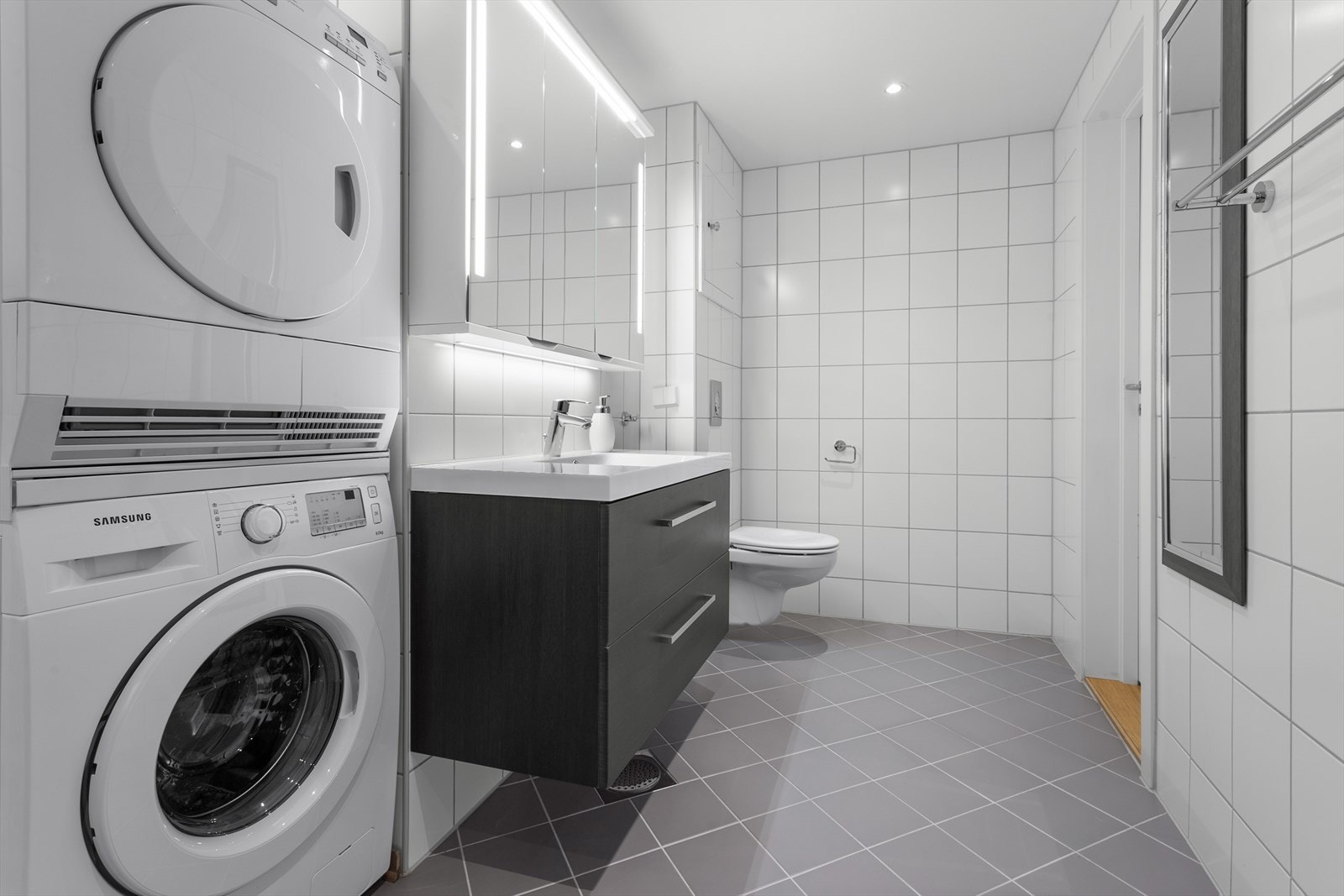 Flislagt med varmekabler i gulv, vegghengt toalett og servant med speilskap over Galleribilde