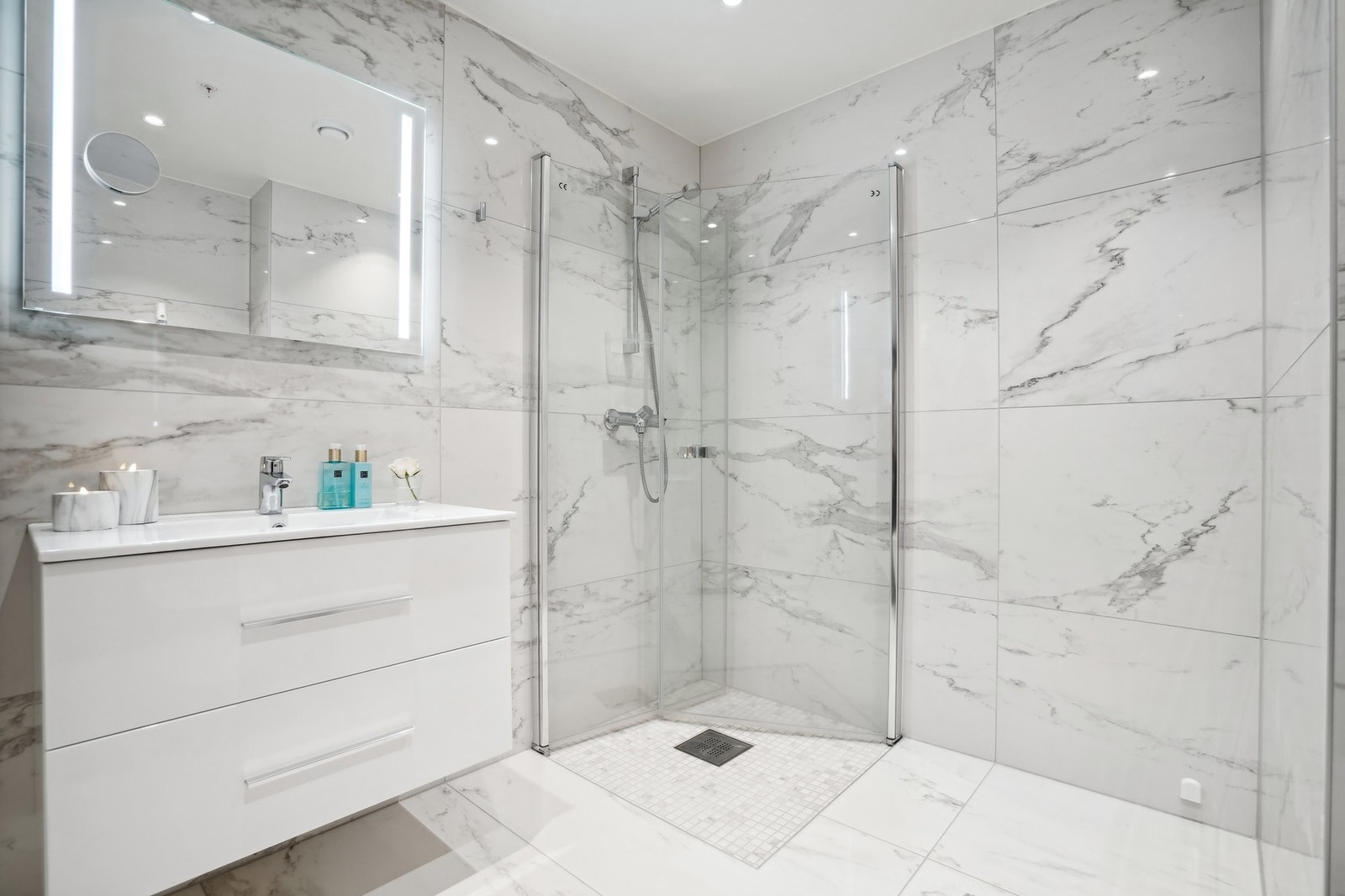 Begge badene er flislagt med elegante "Calacatta Glossy" marmorfliser (60 x 120 cm) og mosaikk i dusj, kombinert med en stilfull sølvgrå fugefarge. Galleribilde