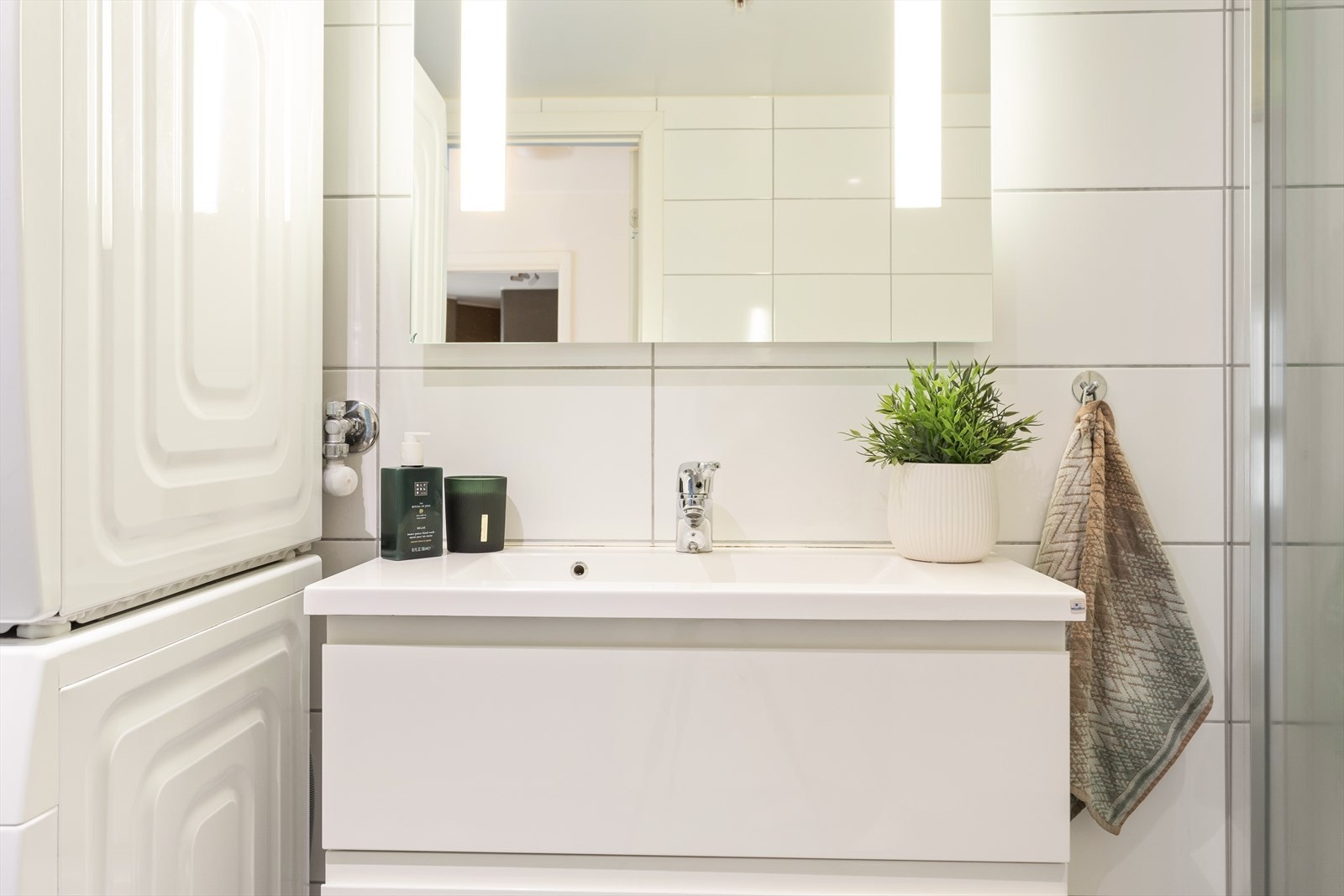 Badet inneholder vegghengt toalett, helstøpt servant, skuffer under servant med slette fronter, dusjdører i klart glass og opplegg for vaskemaskin Galleribilde