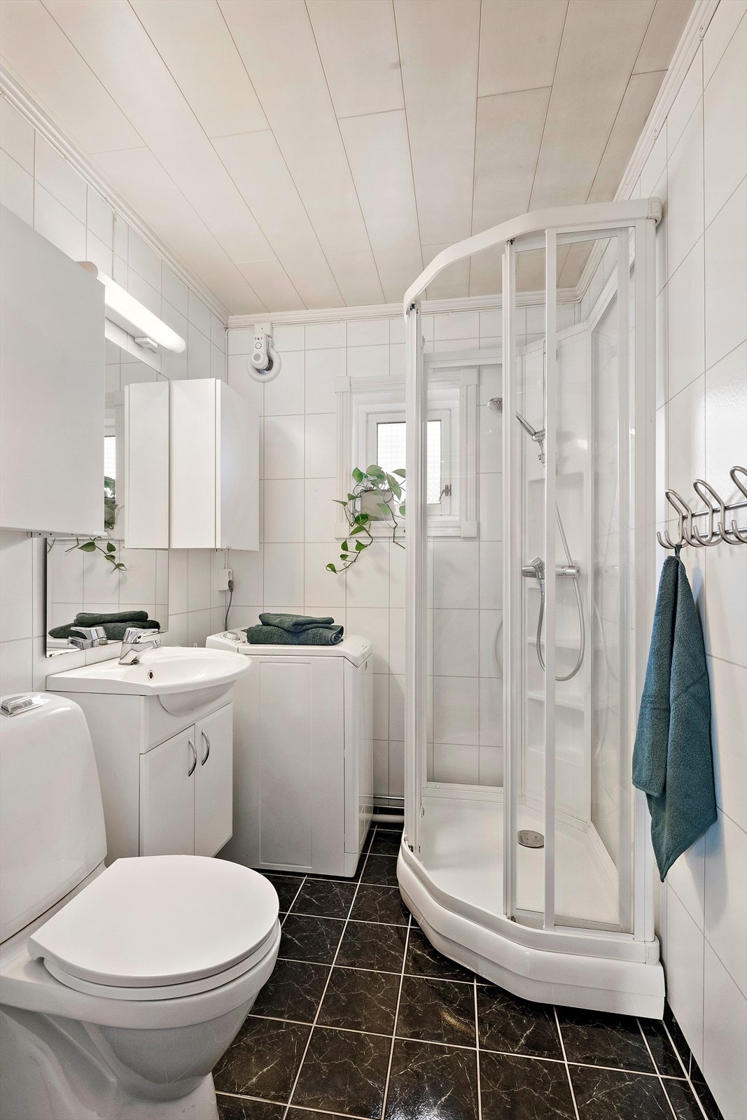Badet inneholder innredning med slette fronter og nedfelt servant, speil og to overskap, toalett, dusjkabinett og opplegg for vaskemaskin. Det er baderomsplater på veggene og trefiberpanel i taket. Gulvet har fliser. Galleribilde
