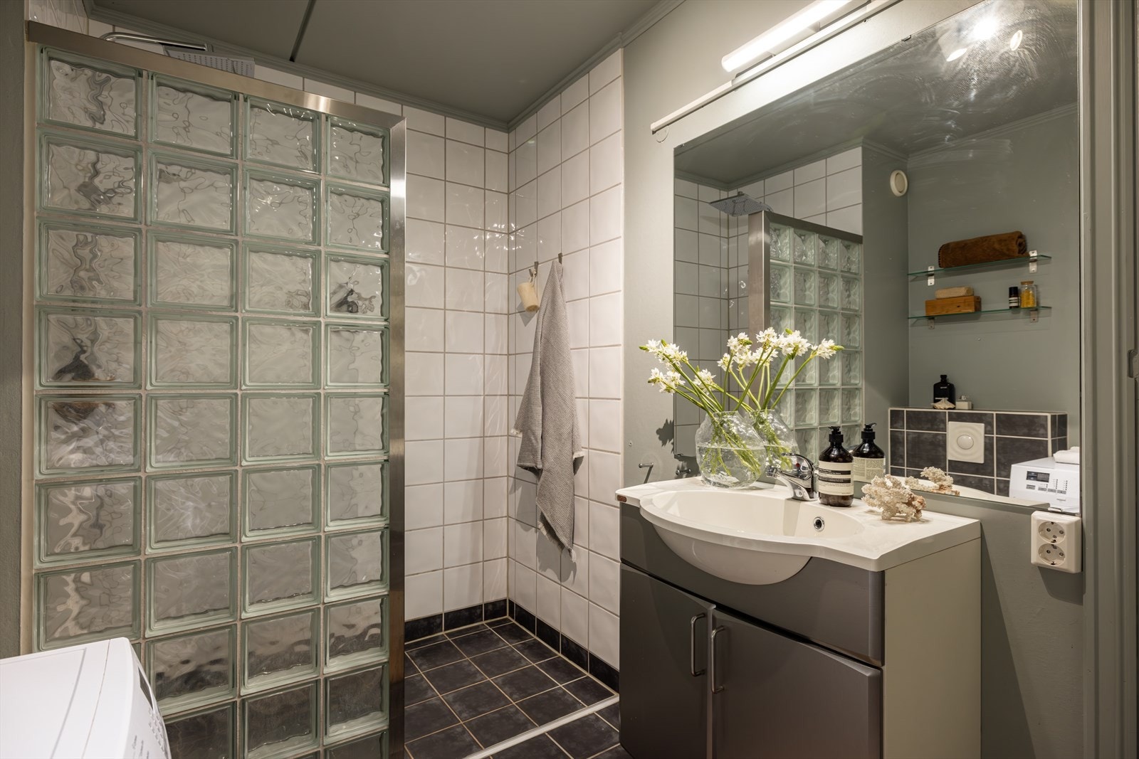 Rommet er innredet med nedfelt servant, veggmontert toalett, dusjvegg av glassbyggerstein og opplegg for vaskemaskin. Galleribilde