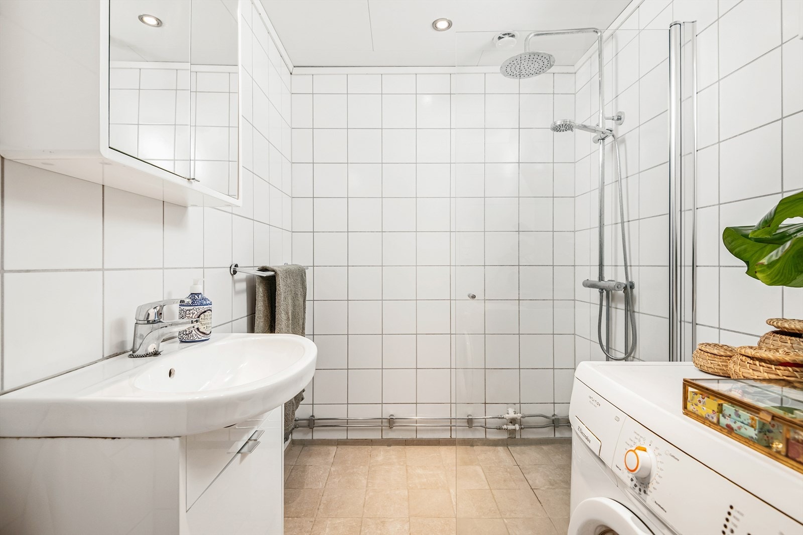 Rommet er innredet med servant med underskap, speil med skap, belysning, dusjvegger og opplegg for vaskemaskin. Galleribilde