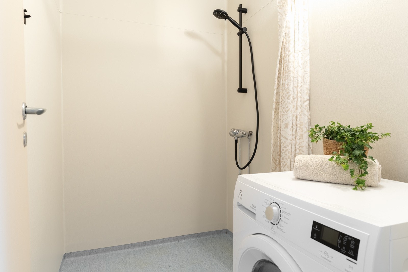 Leilighetens bad har vinyl belegg på gulv og vegger og er innredet med dusj og opplegg for vaskemaskin Galleribilde