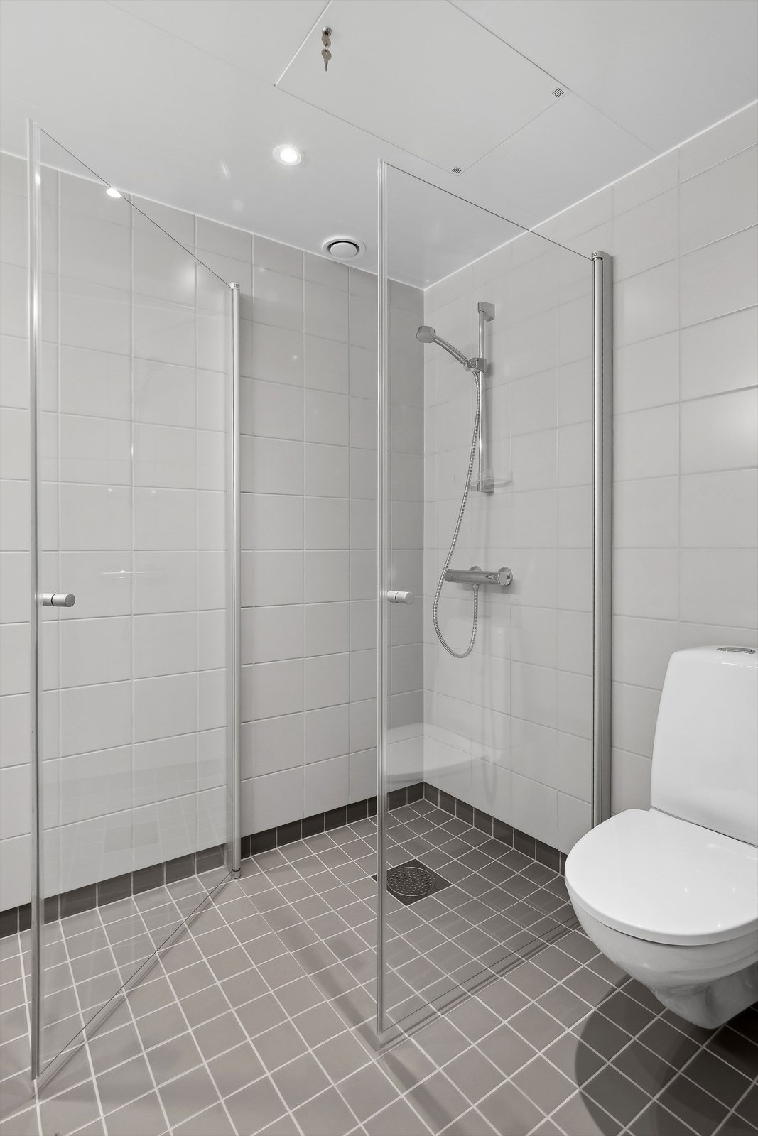 Dusjnisje med innfellbare dusjdører og vegghengt toalett. Galleribilde