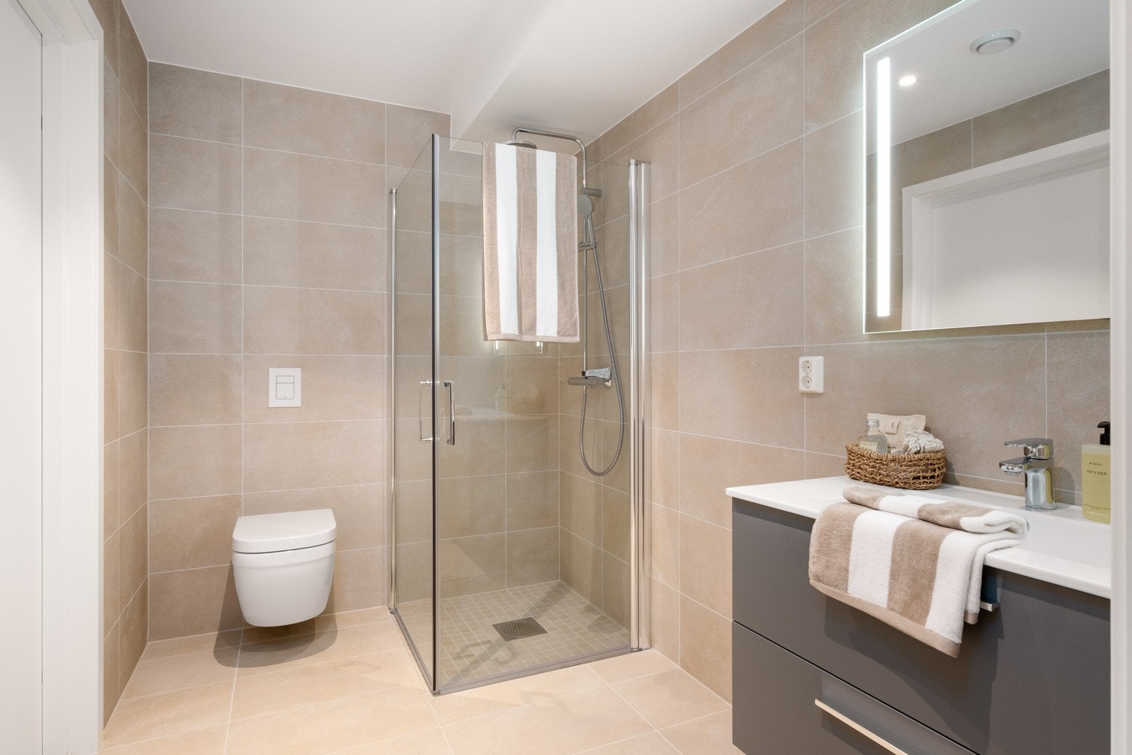 Badet inneholder servantskap med heldekkende servant, innfellbare glassdører, dusjgarnityr og vegghengt toalett. Galleribilde