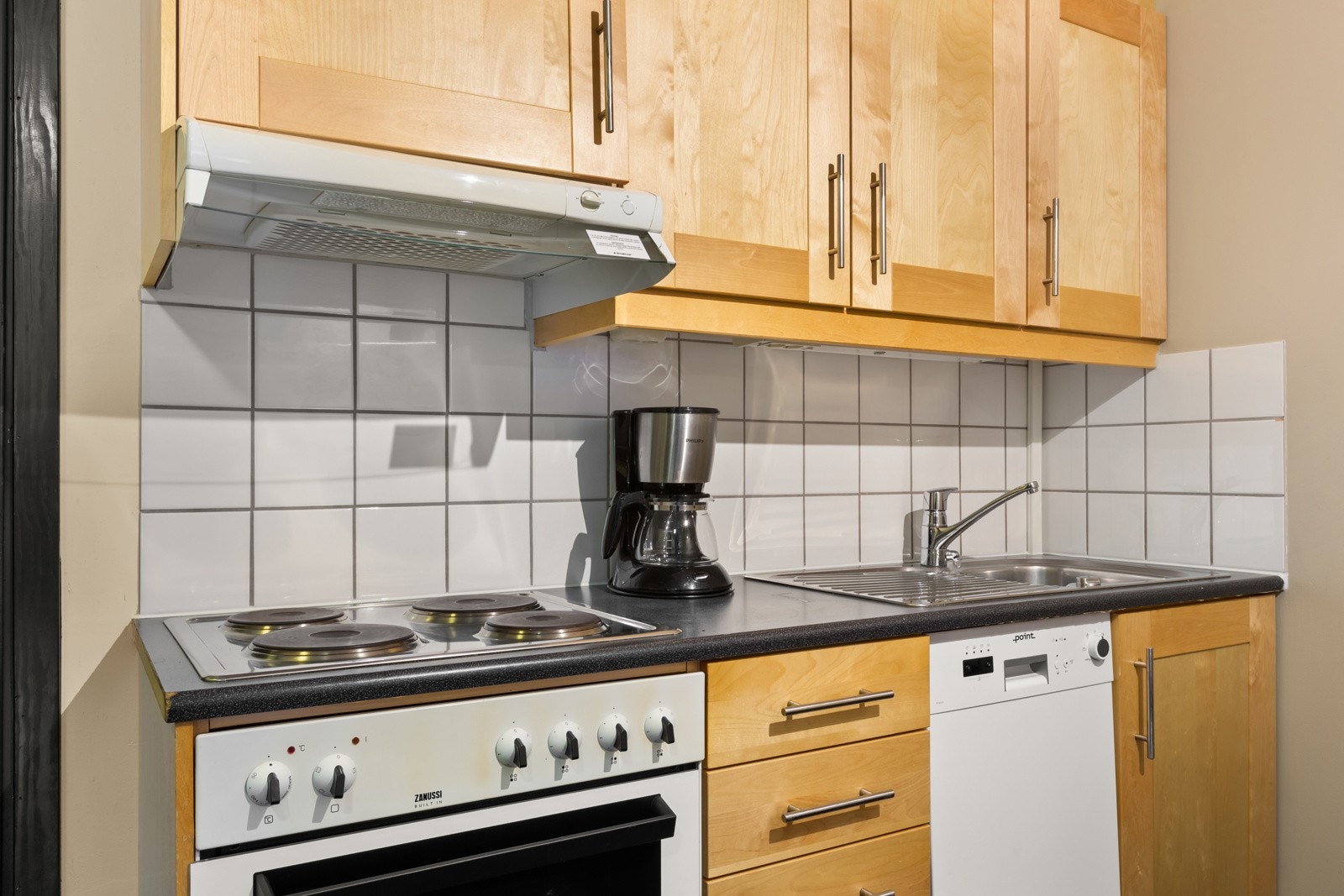 Kjøkkeninnredningen er utført med profilerte fronter, flis mellom benkeplate og overskap og benkeplate av laminat med nedfelt koketopp og oppvaskkum i metall. Galleribilde