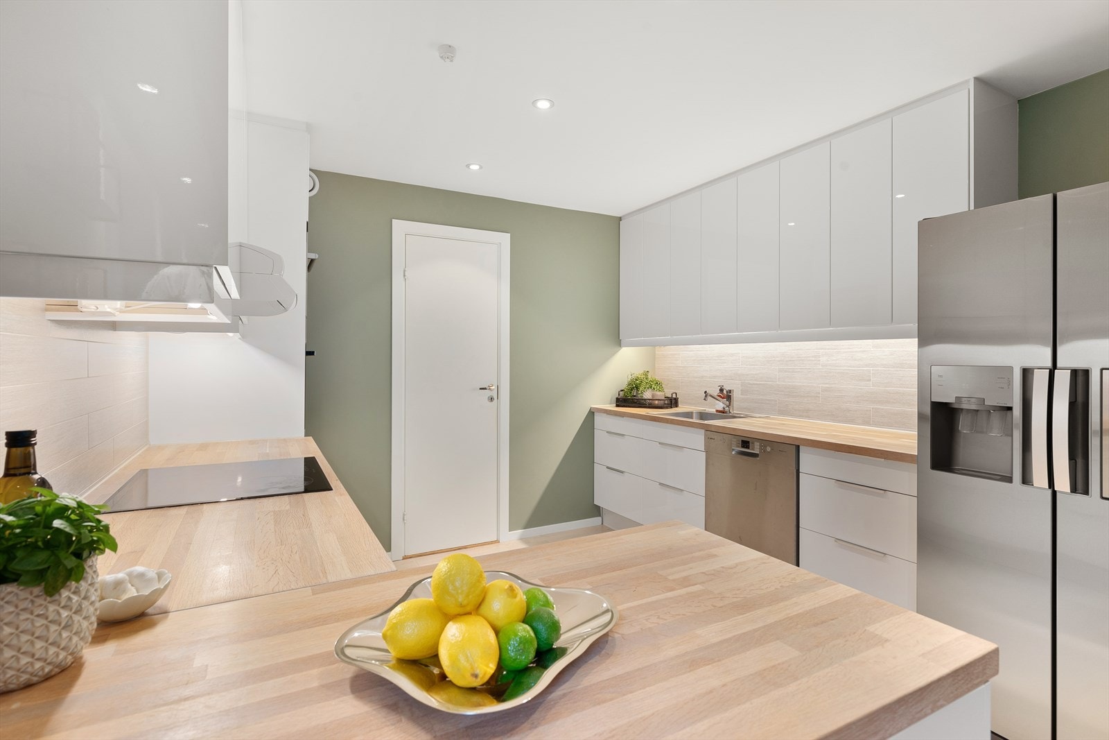 Flissatt felt på vegg mellom overskap og benkeplate. Kjøkkenet har integrerte hvitevarer som koketopp, stekeovn og dampovn som medfølger handelen Galleribilde