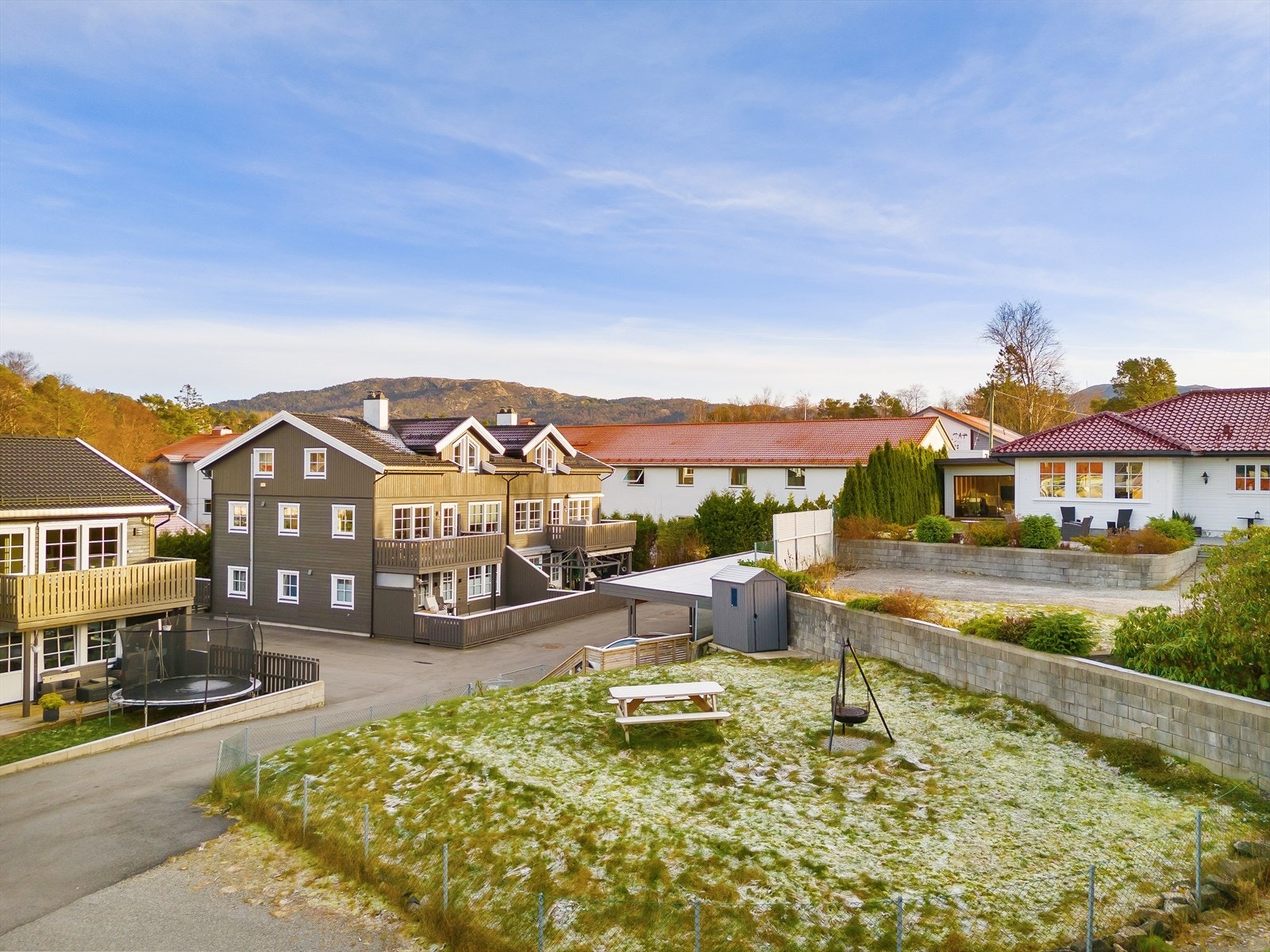 Tomten er pent opparbeidet med asfalt, carporter, boder og plen Galleribilde