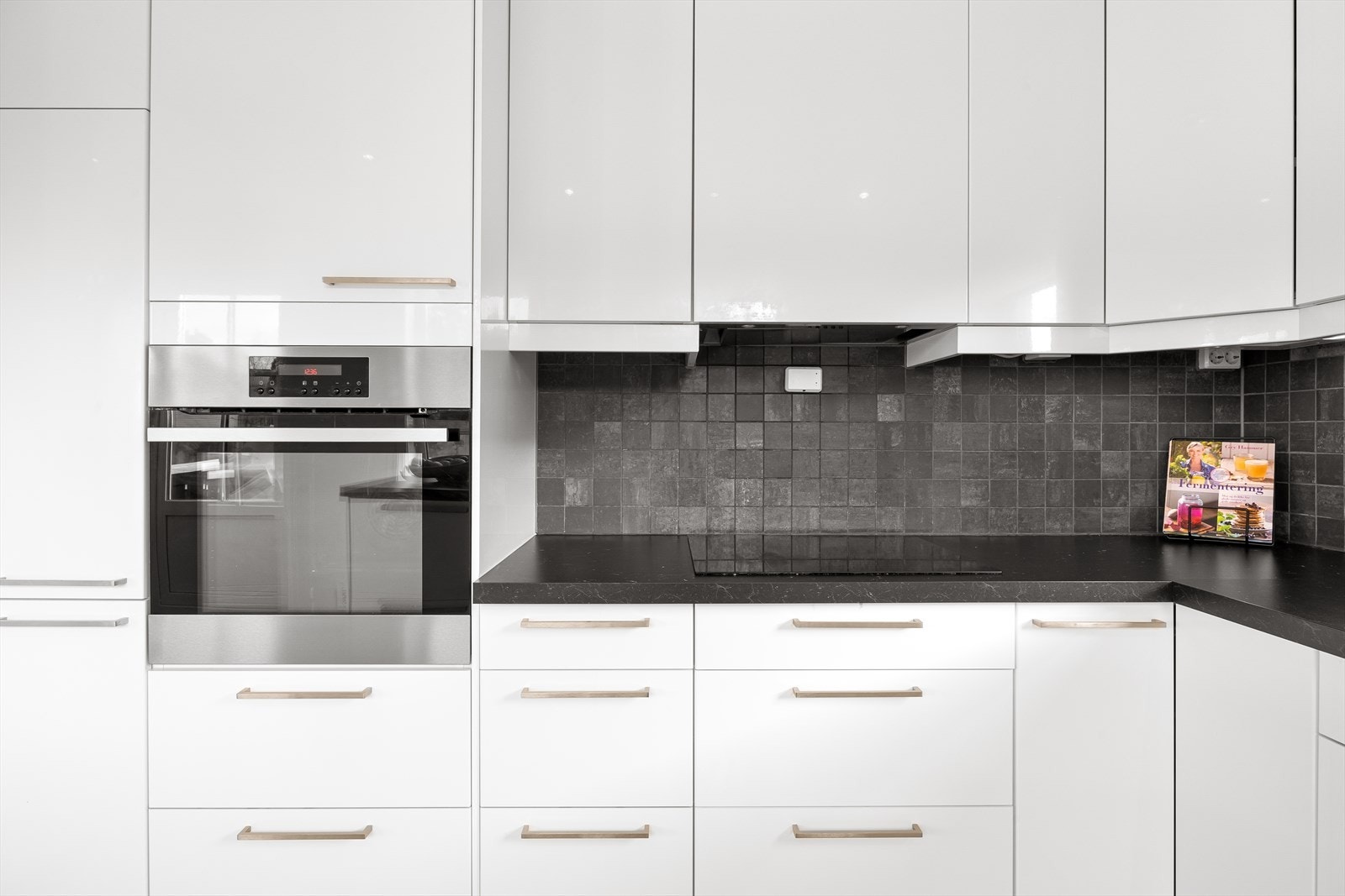 Kjøkken med glatte fronter, benkeplate av laminat, vask, kjøl/fryseskap, oppvaskmaskin, komfyr, platetopp og fliser på bakvegg Galleribilde