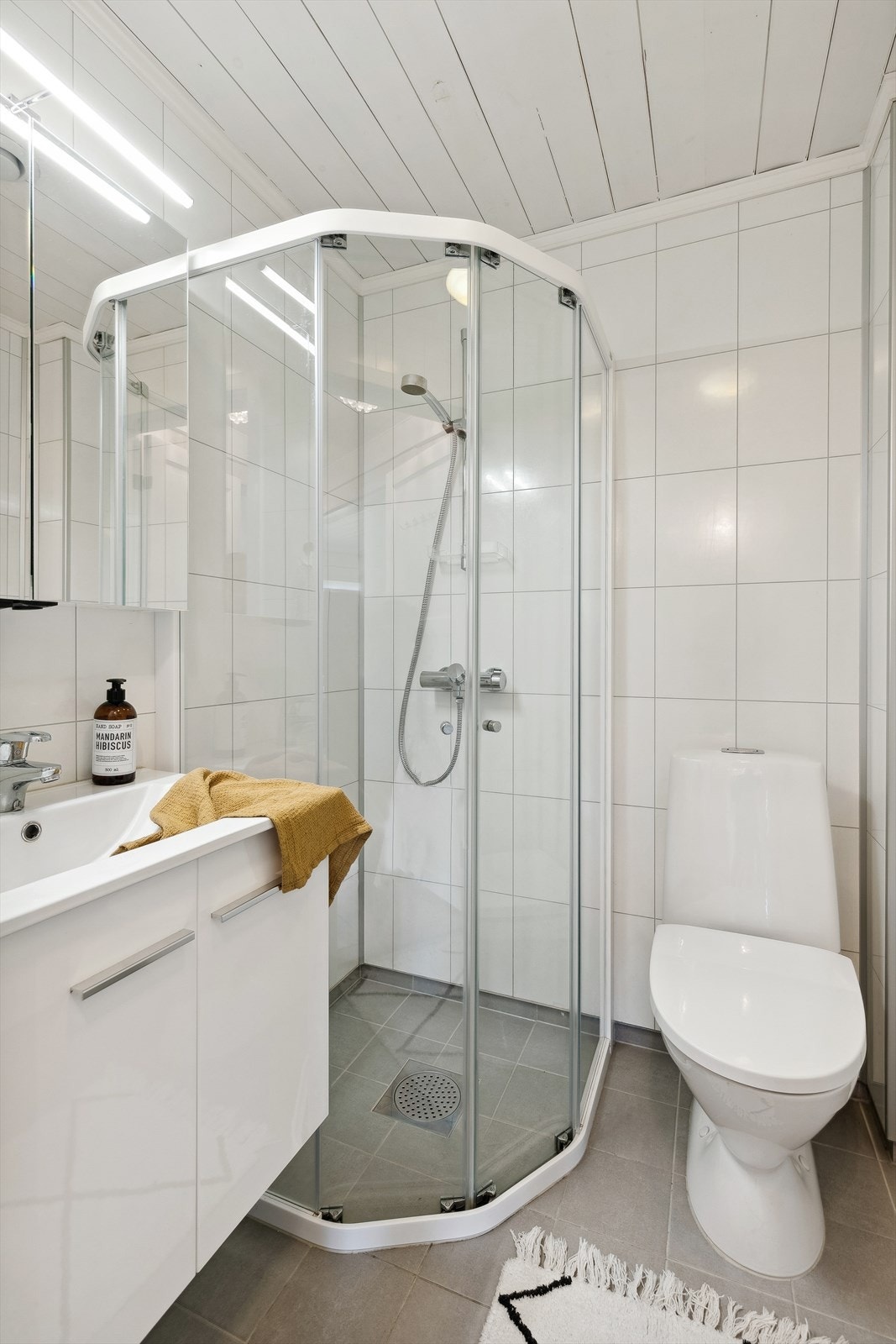 Badet i 1.etg har fliser på gulv og plater på vegg. Innredet med dusjhjørne, wc og baderomsinnredning med heldekkende servant. Galleribilde