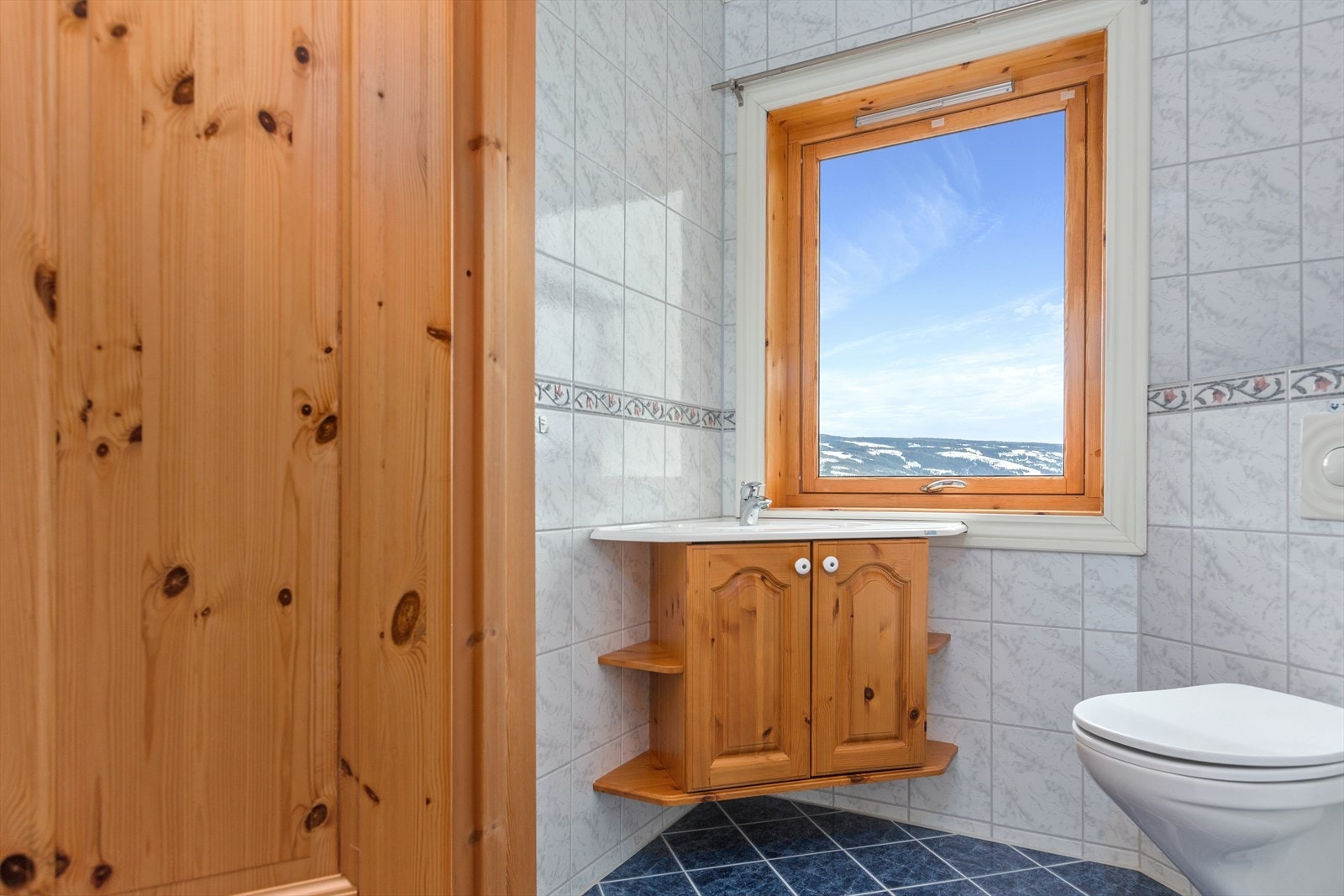 Nær badet er det eget toalettrom, også dette med flislagte vegger og flislagt gulv med varmekabler. På toalettrommet er det heltre servantskap i furu med heldekkende servant, og vegghengt toalett med innfliset sisterne. Galleribilde
