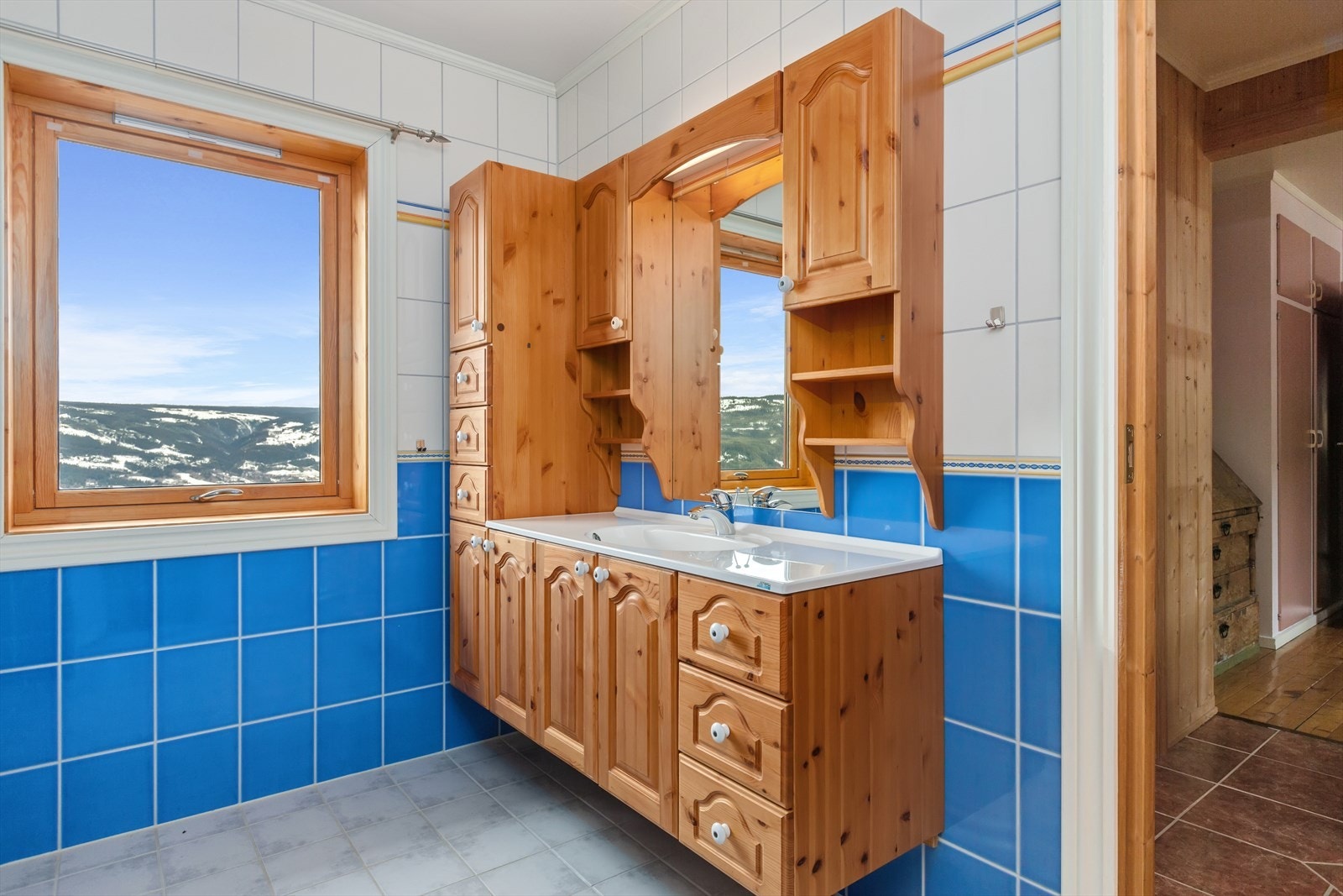 Det flislagte badet med varmekabler i gulv er fra 2002. Her er det downlights belysning og heltre baderomsinnredning med over- og underskap, høyskap og speil. Dusj med forheng og blandebatteri for badekar. Galleribilde