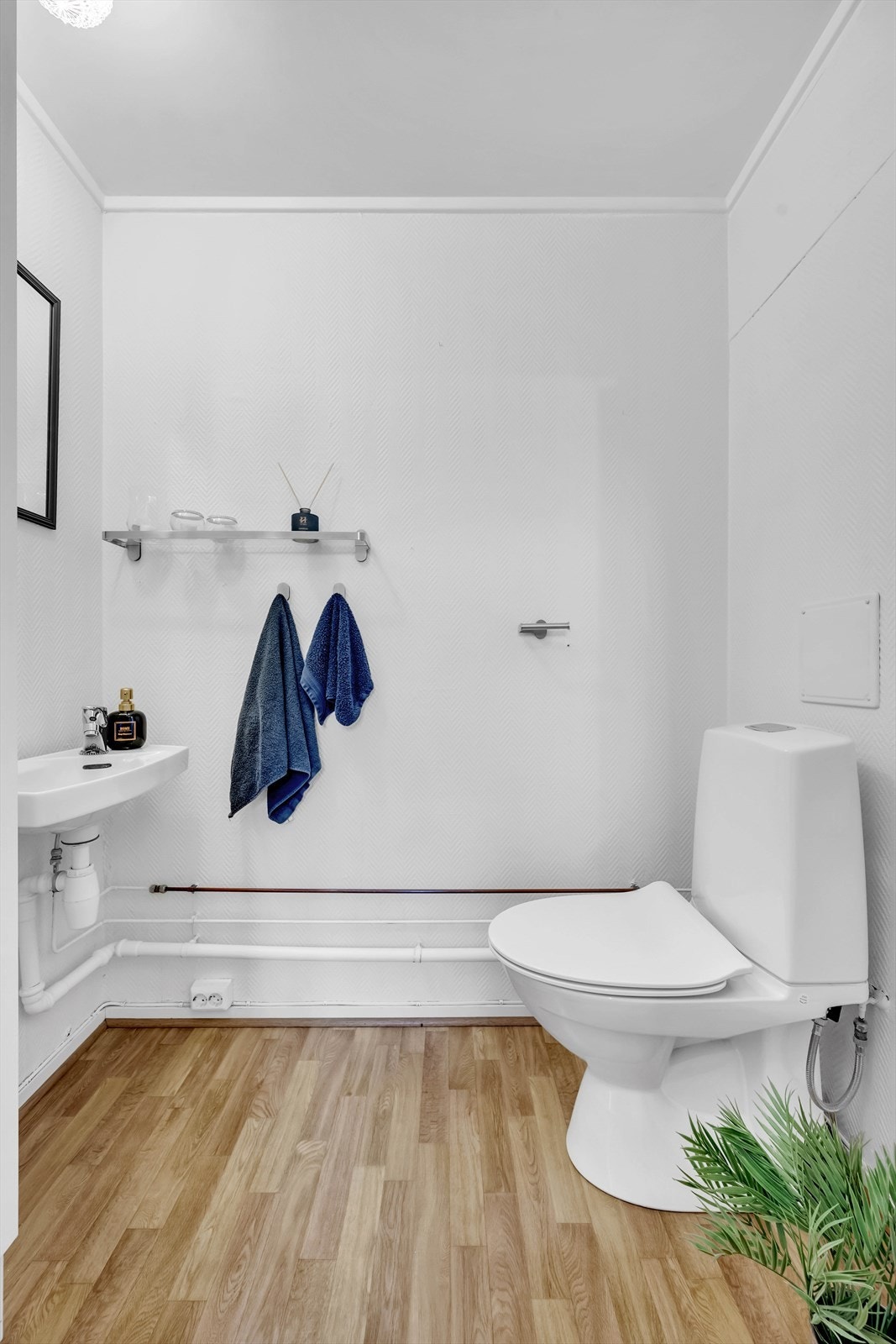 Praktisk toalettrom med malt fiskebensstrie på vegger og vinylbelegg på gulv. Rommet er innredet med klosett og servant. Naturlig ventilasjon. Galleribilde
