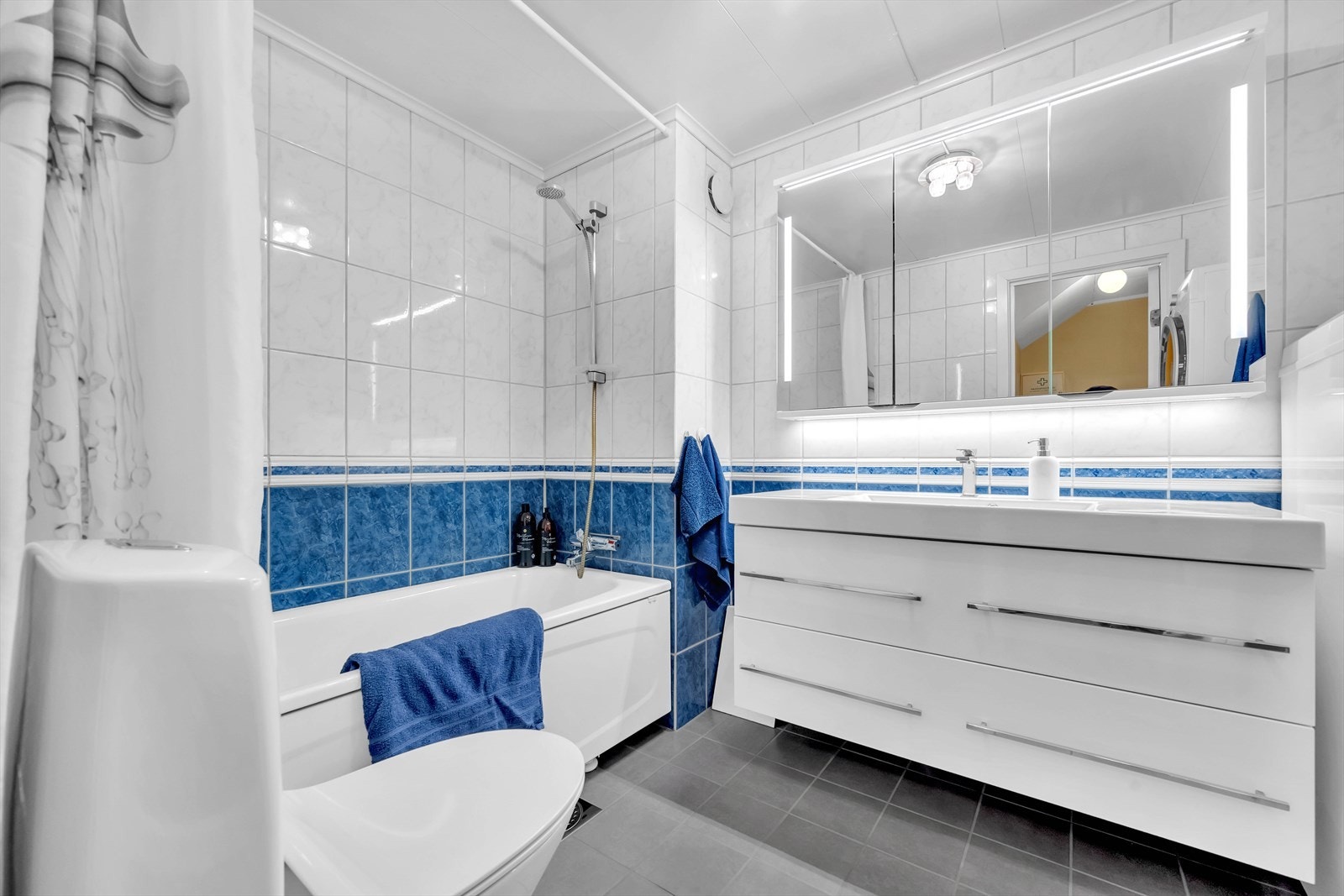 Badet er innredet med toalett, servant nedfelt i innredning, speilskap med lys og badekar. Galleribilde