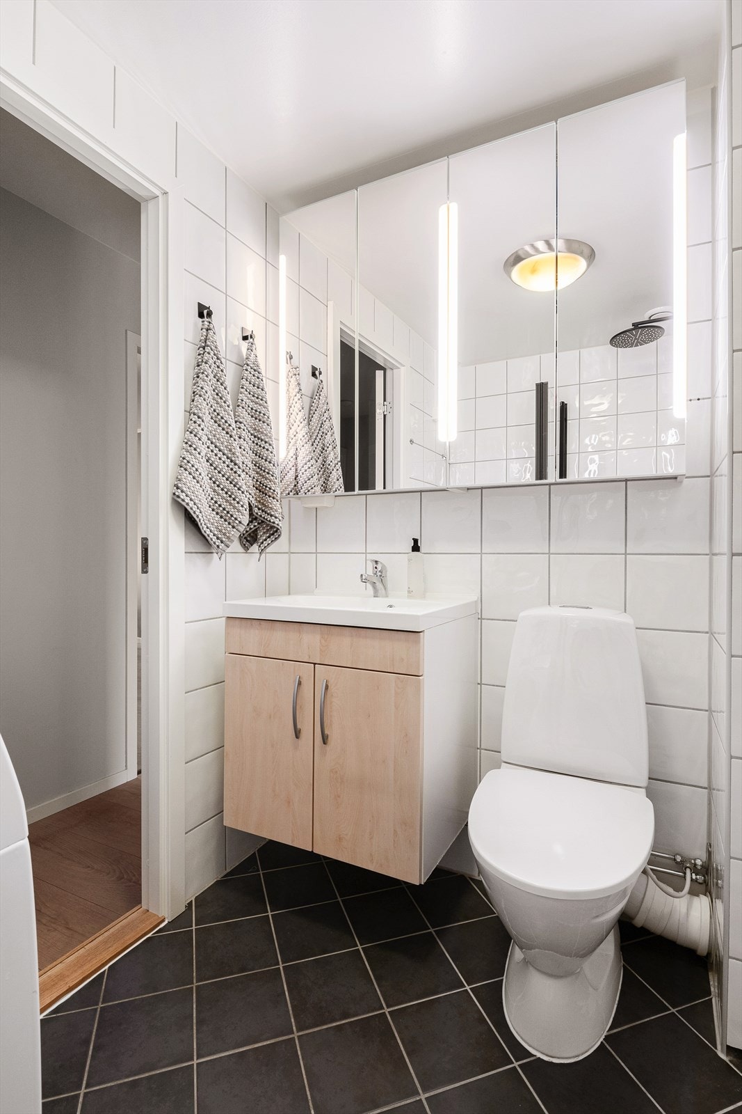 Flislagt bad med varmekabler i gulv. Inneholder dusjhjørne, opplegg for vaskemaskin, toalett, servant og speilskap Galleribilde