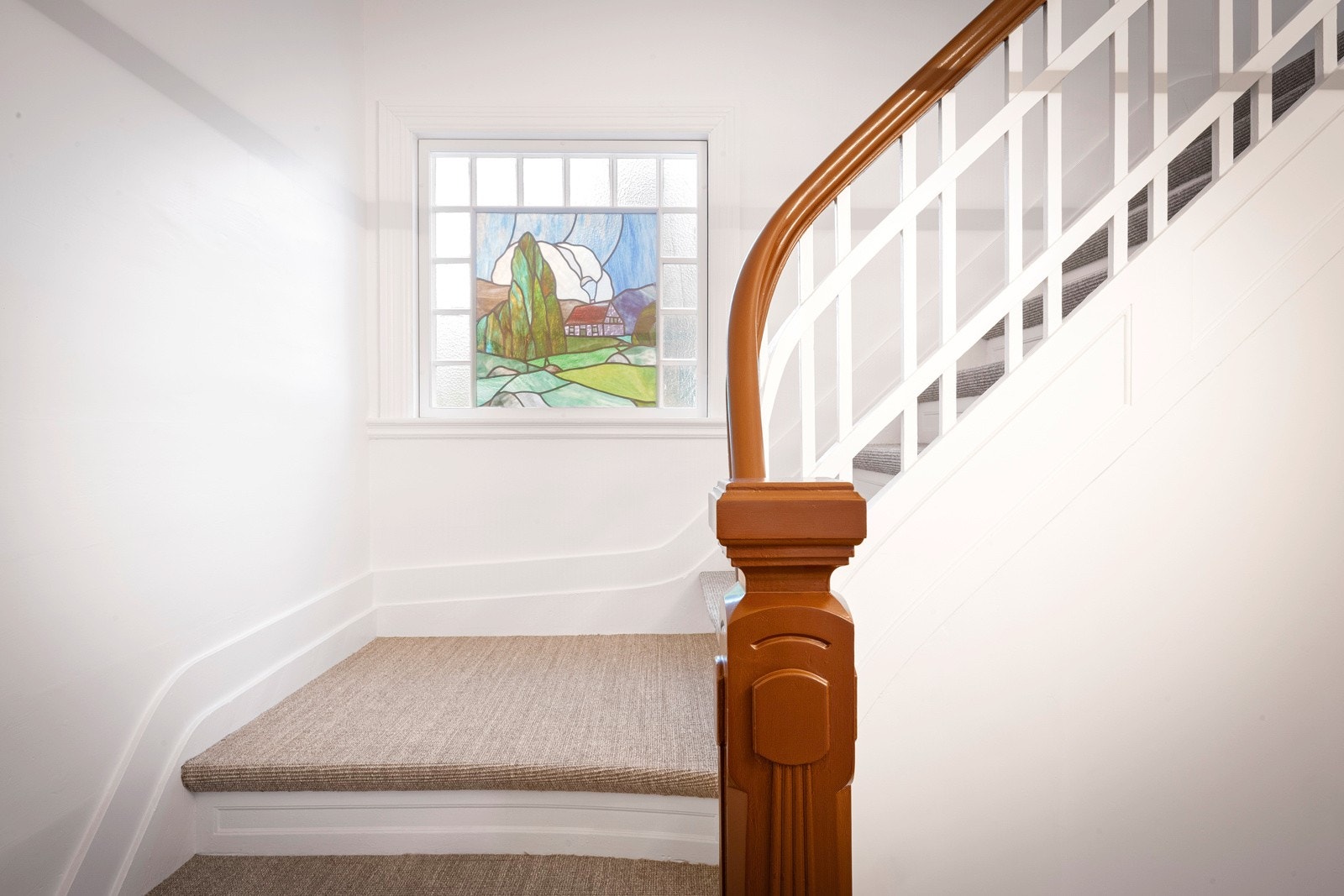 Midt i trappen er det et blyglassvindu med dekorativt motiv og veggene er hvitmalt. Galleribilde
