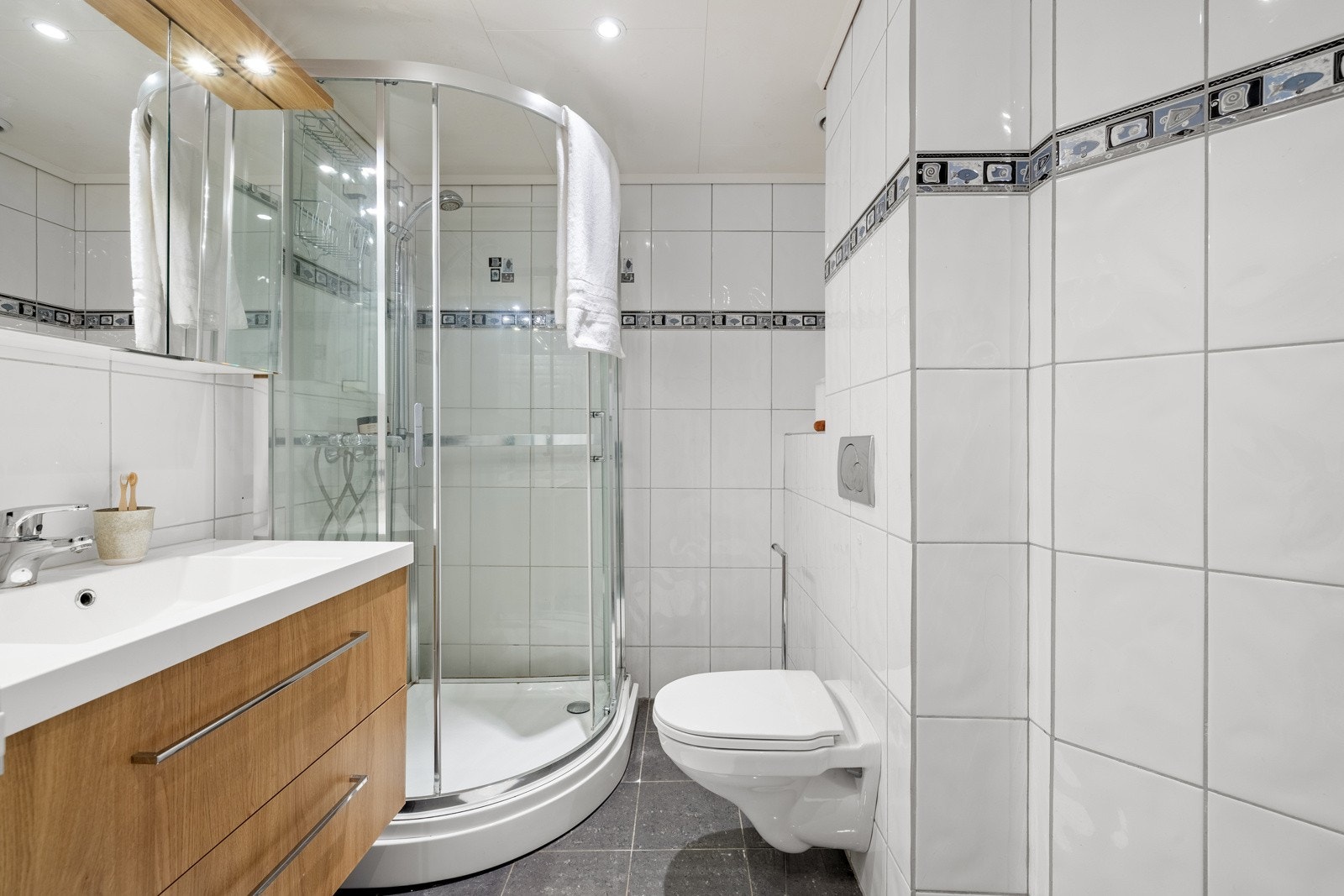 Badet er innredet med baderomsinnredning, vegghengt toalett, dusj med glassdører og opplegg for vaskemaskin. Galleribilde