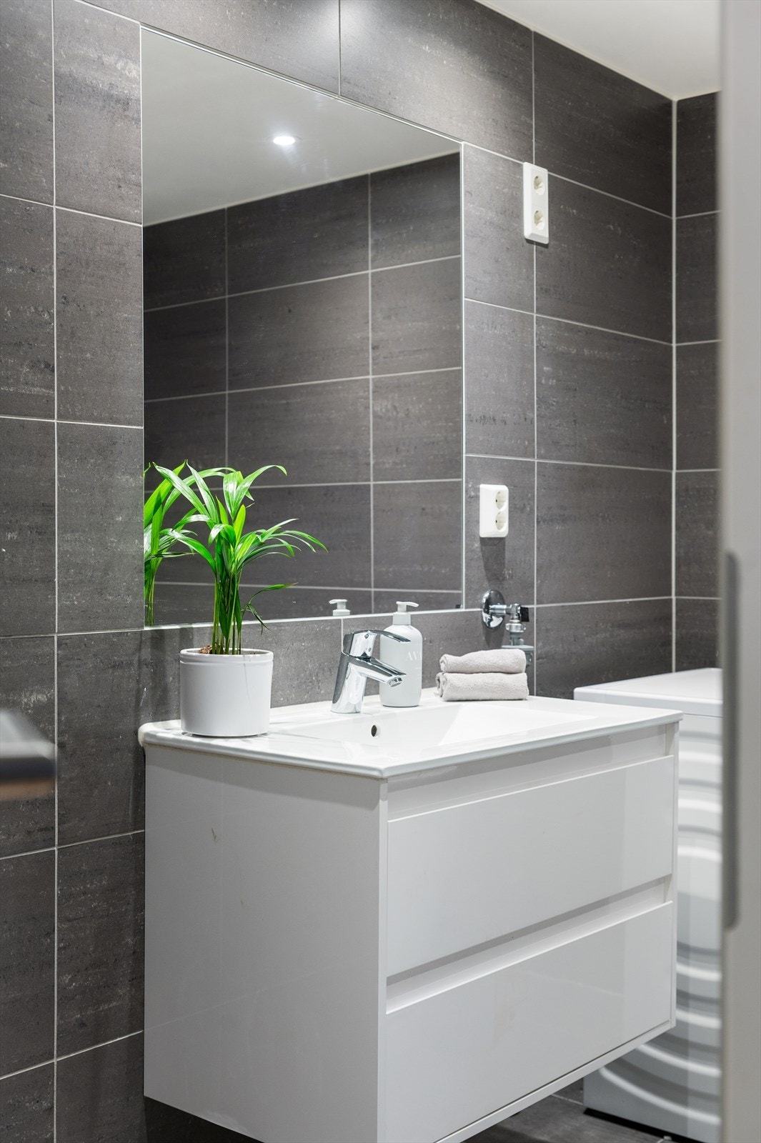 Badet er innredet med vegghengt toalett, servant nedfelt i innredning, speil over servant og dusjhjørne med badekar. Det er opplegg for vaskemaskin og avtrekksventil for mekanisk avtrekk er plassert i himling. Galleribilde