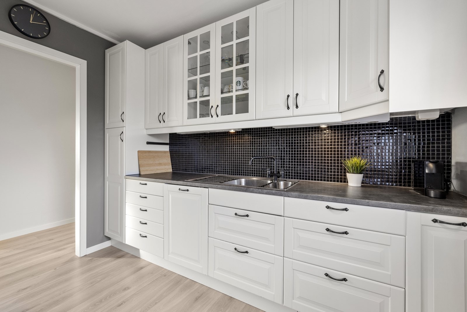 Kjøkkeninnredningen er lys med profilerte fronter, mørk benkeplate og det er lagt fliser mellom overskap og benkeplate. Galleribilde