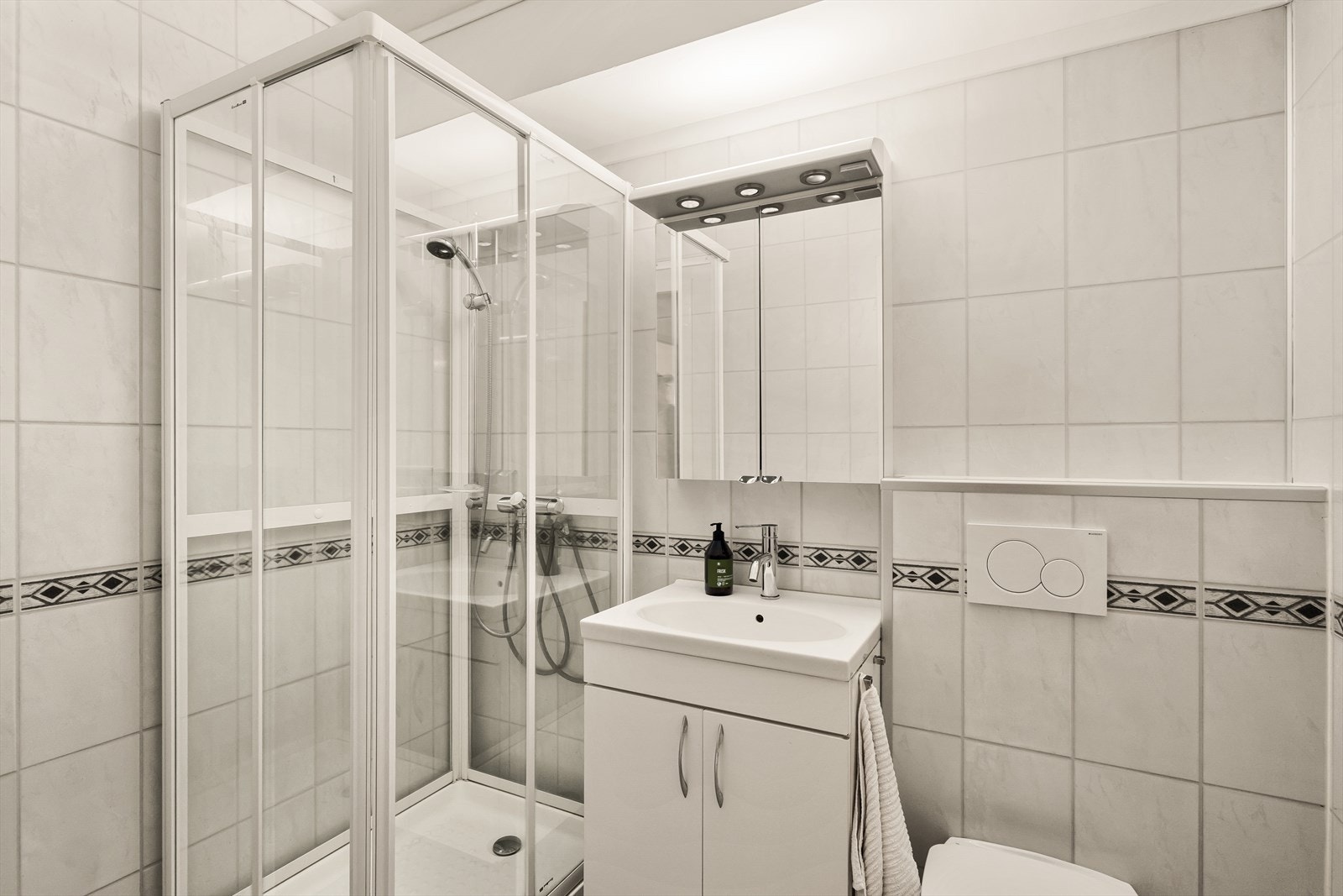 Badet har baderomsplater på vegger og belegg på gulv. Innredet med veggmontert wc, servant og dusjkabinett. Rommet var antakelig pusset opp for 10-15 år siden Galleribilde