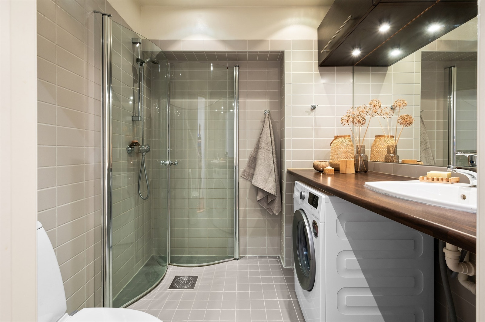 Baderommet er flislagt i nøytrale farger med grå og beige fliser på henholdsvis gulv og vegger og byr på gulvvarme, downlights i himling samt. opplegg for vaskemaskin. Galleribilde