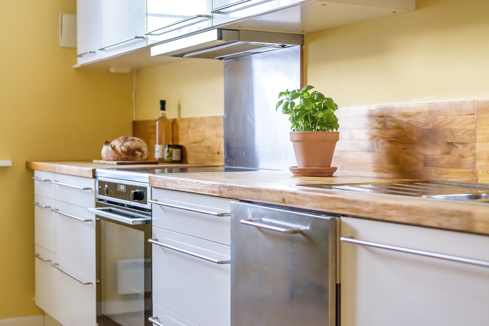 En stilren, hvit kjøkkeninnredning med glatte fronter og benkeplate av heltre. Galleribilde