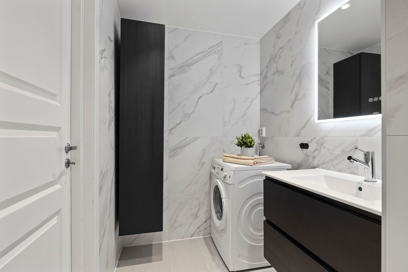 Baderomsinnredningen er i sort utførelse og består av et veggmontert høyskap, skuffeseksjon med heldekkende servant og et like bredt speil med integrert belysning Galleribilde