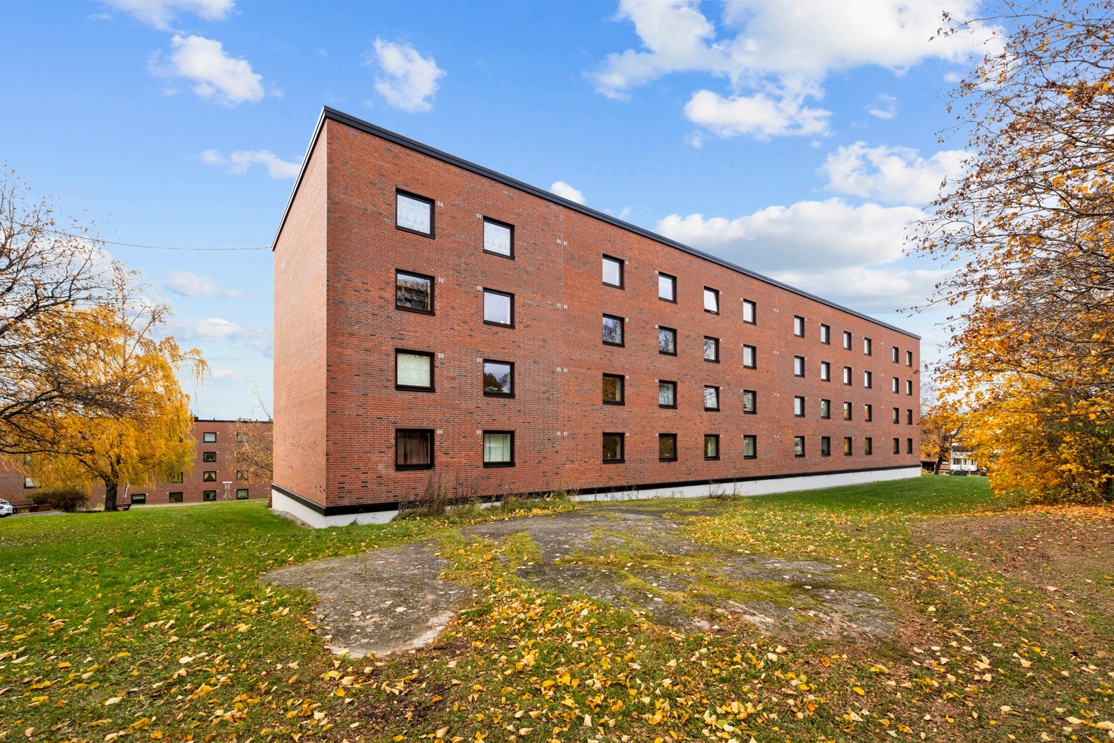 På bakkeplan har borettslaget et lett skrånende tomt med store grøntareal, noe fjell, trær, prydbusker og hekker Galleribilde