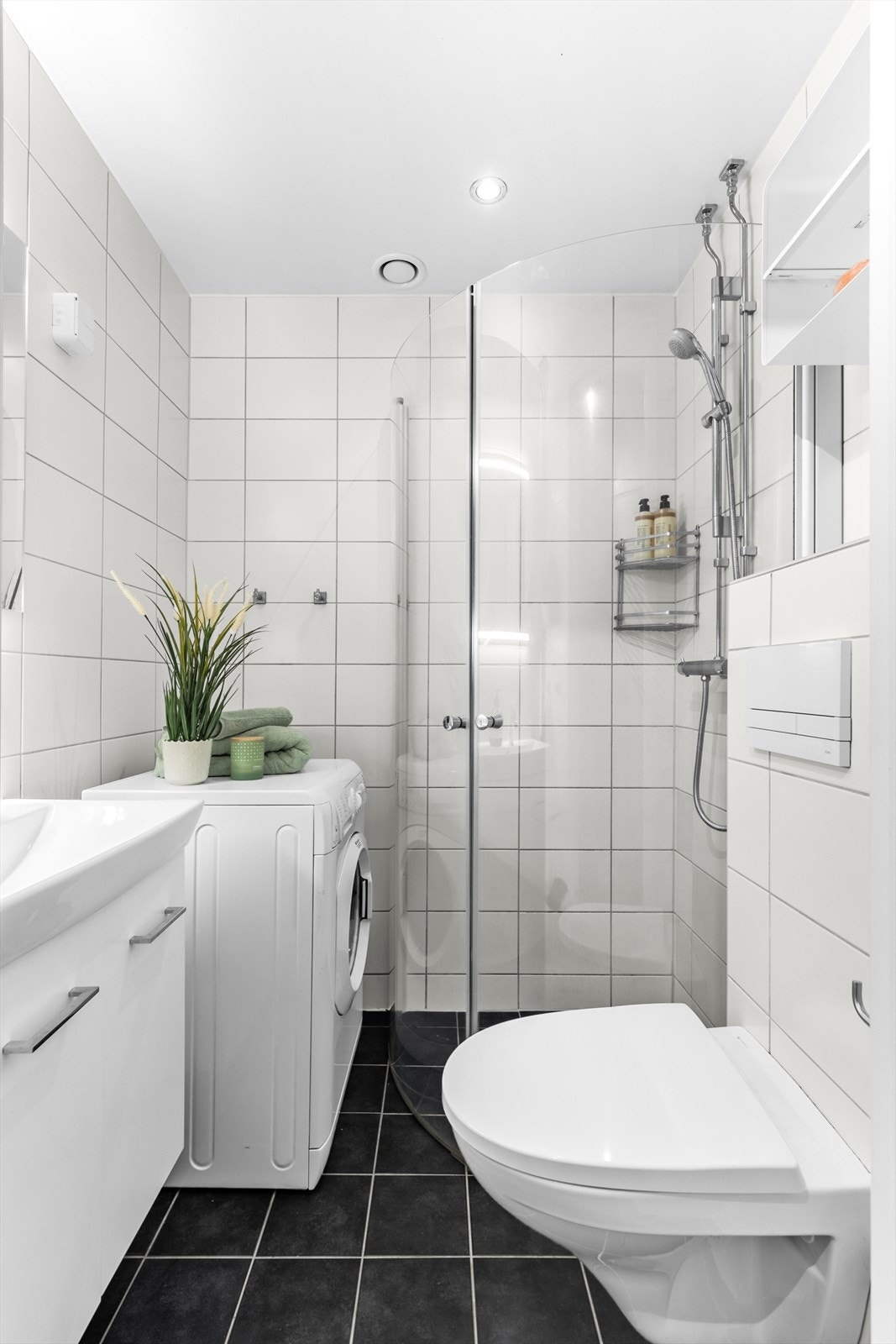 Badet er innredet med vegghengt klosett, servant med innredning, speil med lys og dusjhjørne med svingbare glassdører. Galleribilde