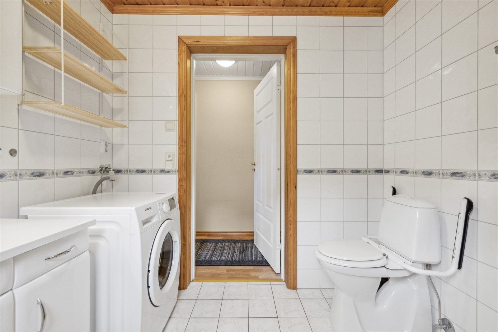 Lyst og pent baderom med fliser på vegg og gulv, samt varmekabler i gulv. Baderommet har dusj på vegg med innfellbare glassdører, baderomsinnredning med formstøpt vask, toalett og opplegg til vaskemaskin. Galleribilde