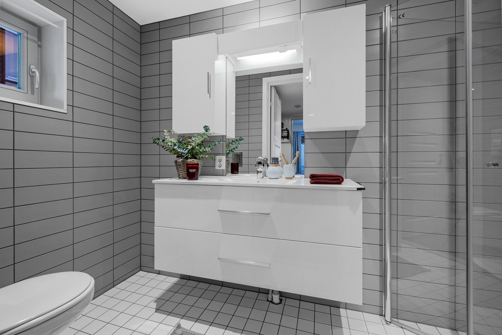 Leiligheten har totalt 2 bad. Dette badet har flislagt gulv og vegger og er innredet med servantskap, overskap med speil, toalett og dusjvegger. Galleribilde