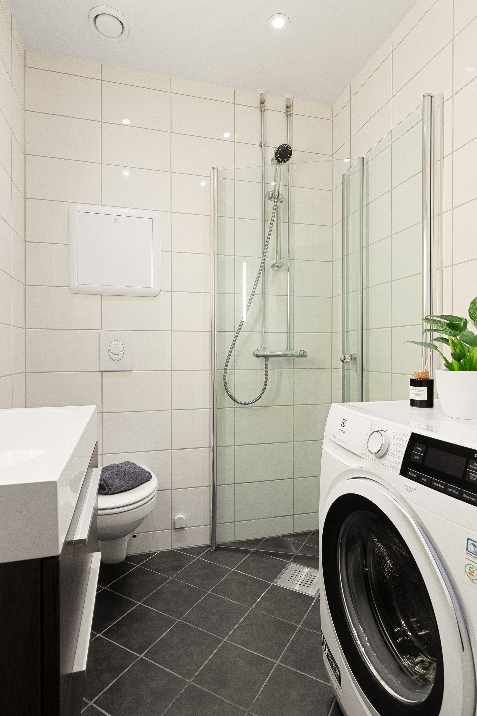 Baderommet inneholder dusjhjørne med innfellbare svingdører, benkeskap med heldekkende servant, toalett og opplegg for vaskemaskin/tørketrommel. Galleribilde