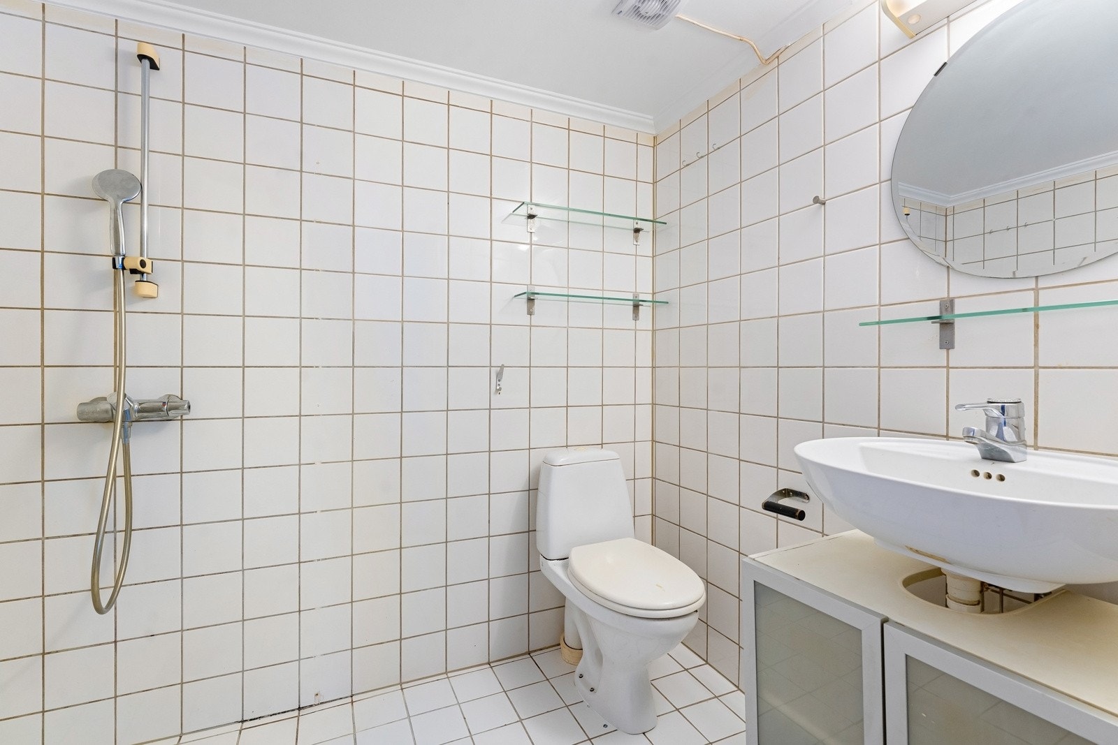 Baderommet har flislagte flater og dusj, wc og servant med speildel og underskap Galleribilde