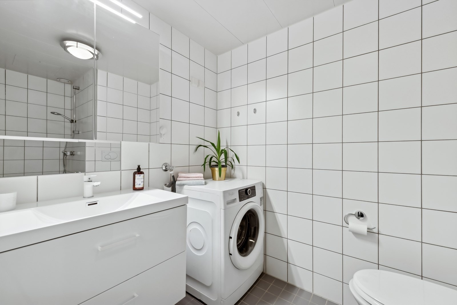 Helfliset og pent bad med dusjnisje, baderomsinnredning med speil, vegghengt WC og opplegg for vaskemaskin. Galleribilde