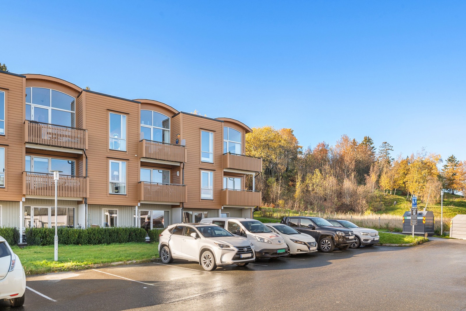 Fasade og felles oppstillingsplasser for bil. Boligen ligger i blindvei, grensende til friområde. Galleribilde