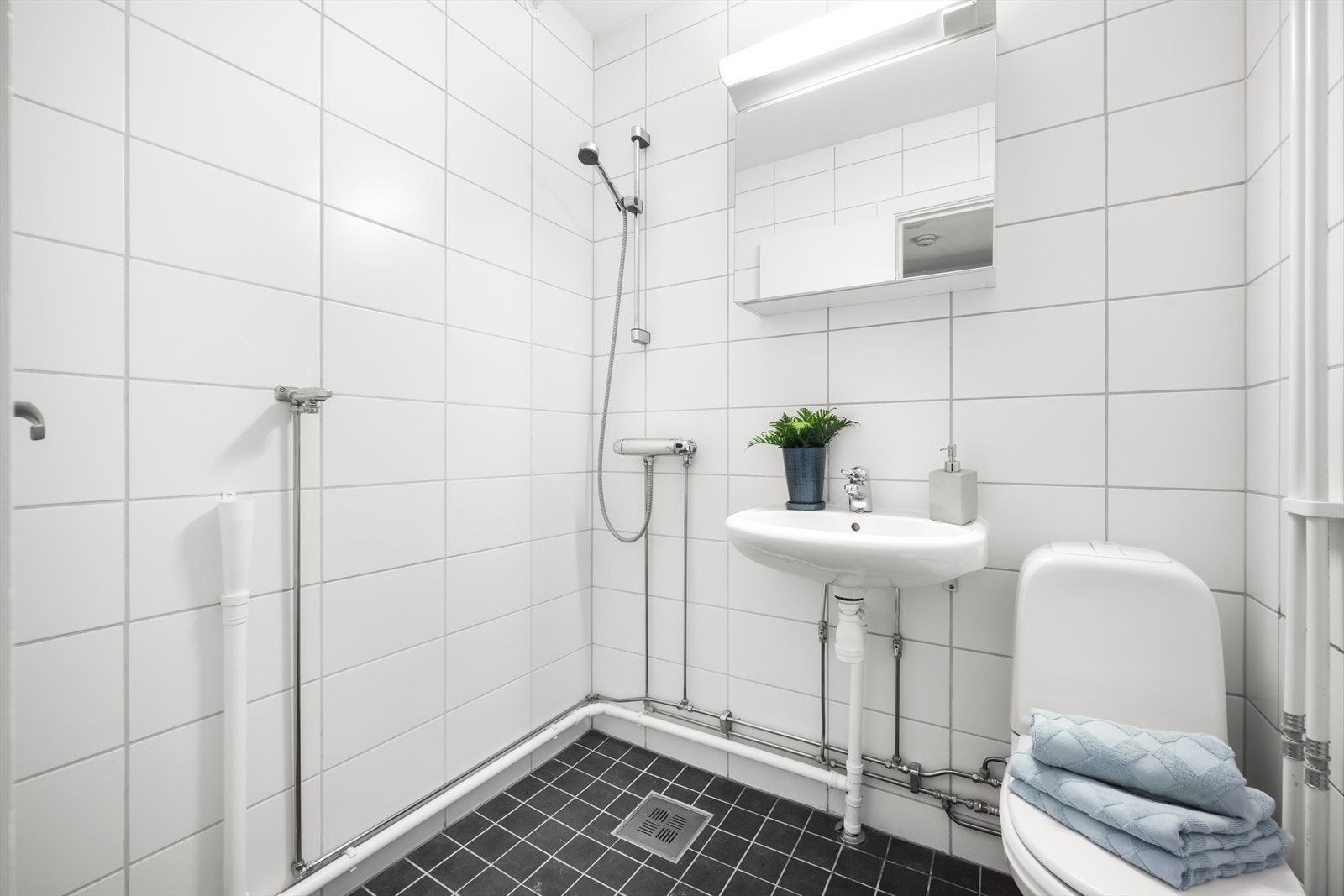 Flislagt baderom med frittstående toalett, vegghengt servant, speilskap med lys. Det er opplegg for vaskemaskin. Galleribilde